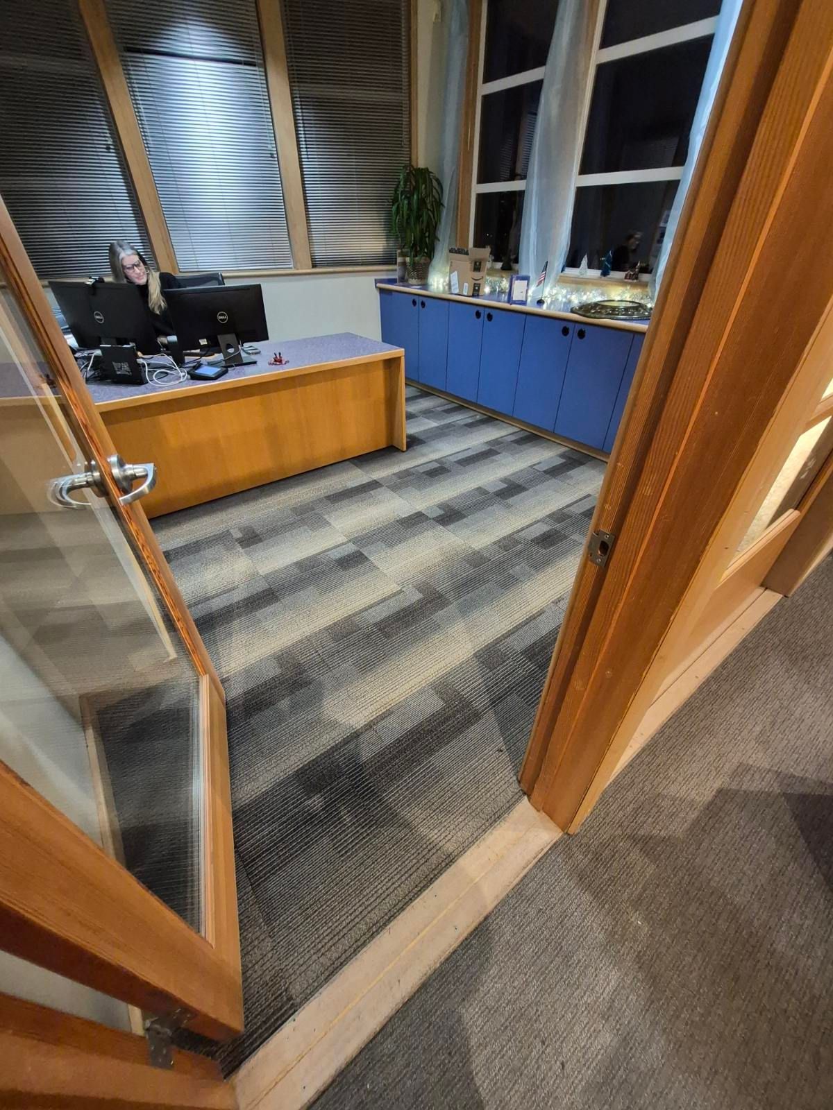 Office interior with wood trim, desk, blue cabinets, and a person working at a computer.