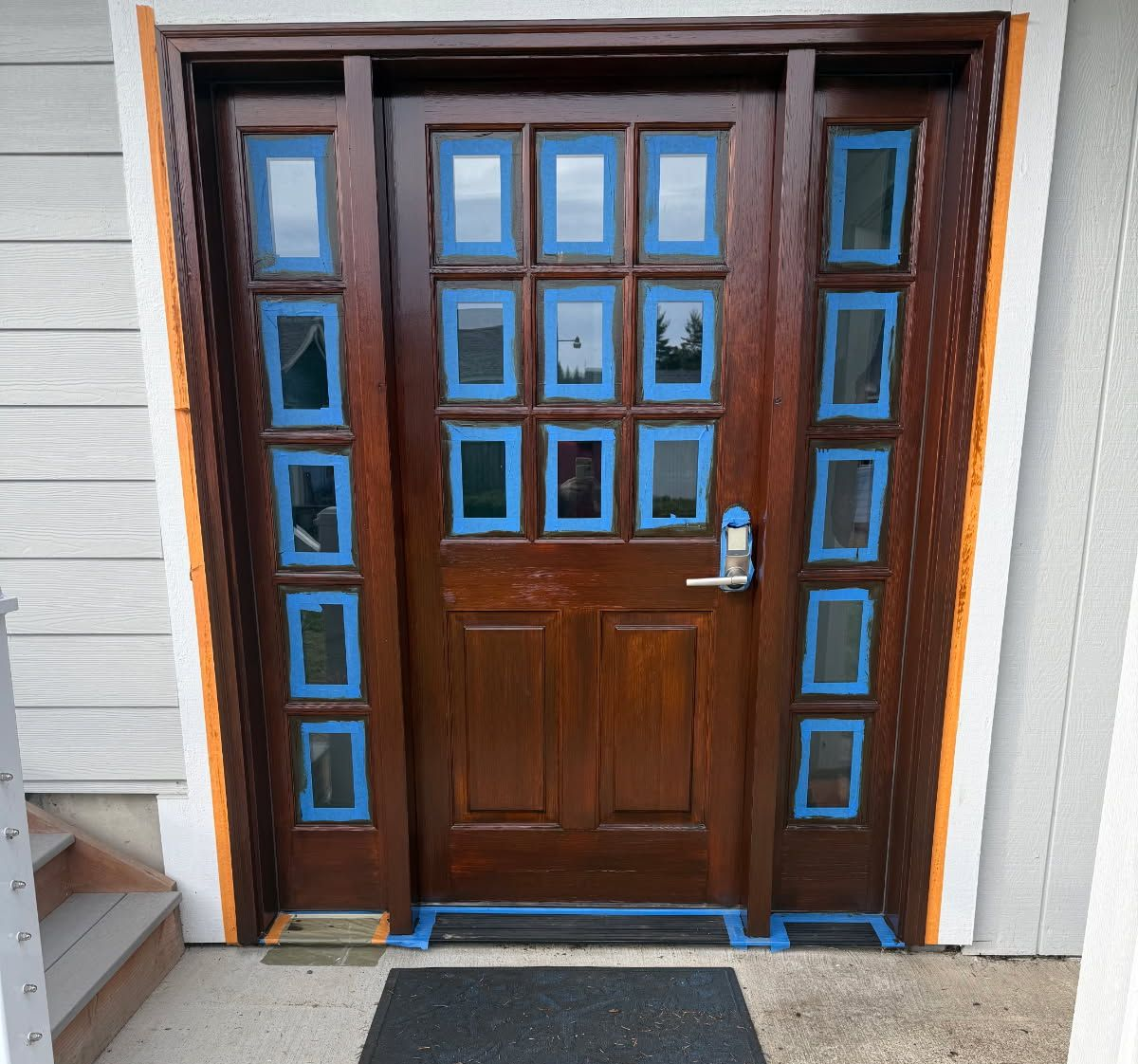 Wooden front door with windows, taped for painting; exterior setting.