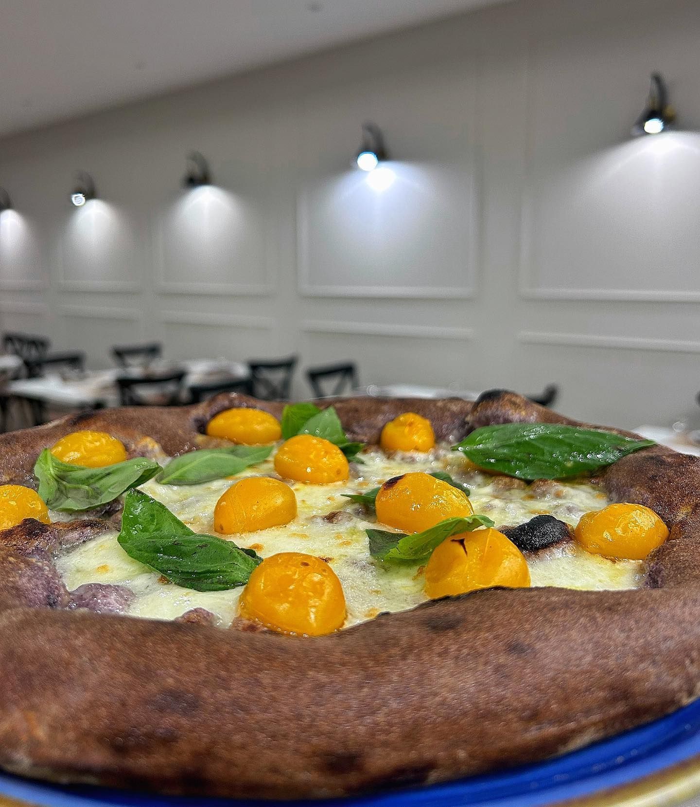 Una pizza con pomodori e basilico su un piatto blu in un ristorante.