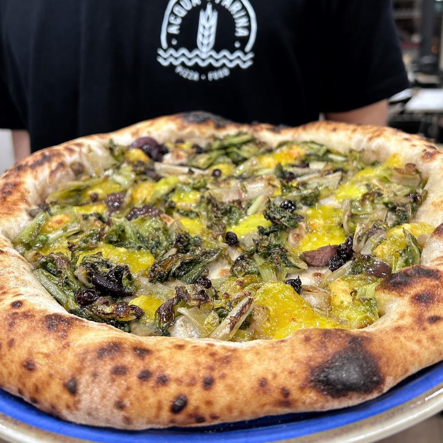 Una persona tiene in mano una pizza su un piatto blu.