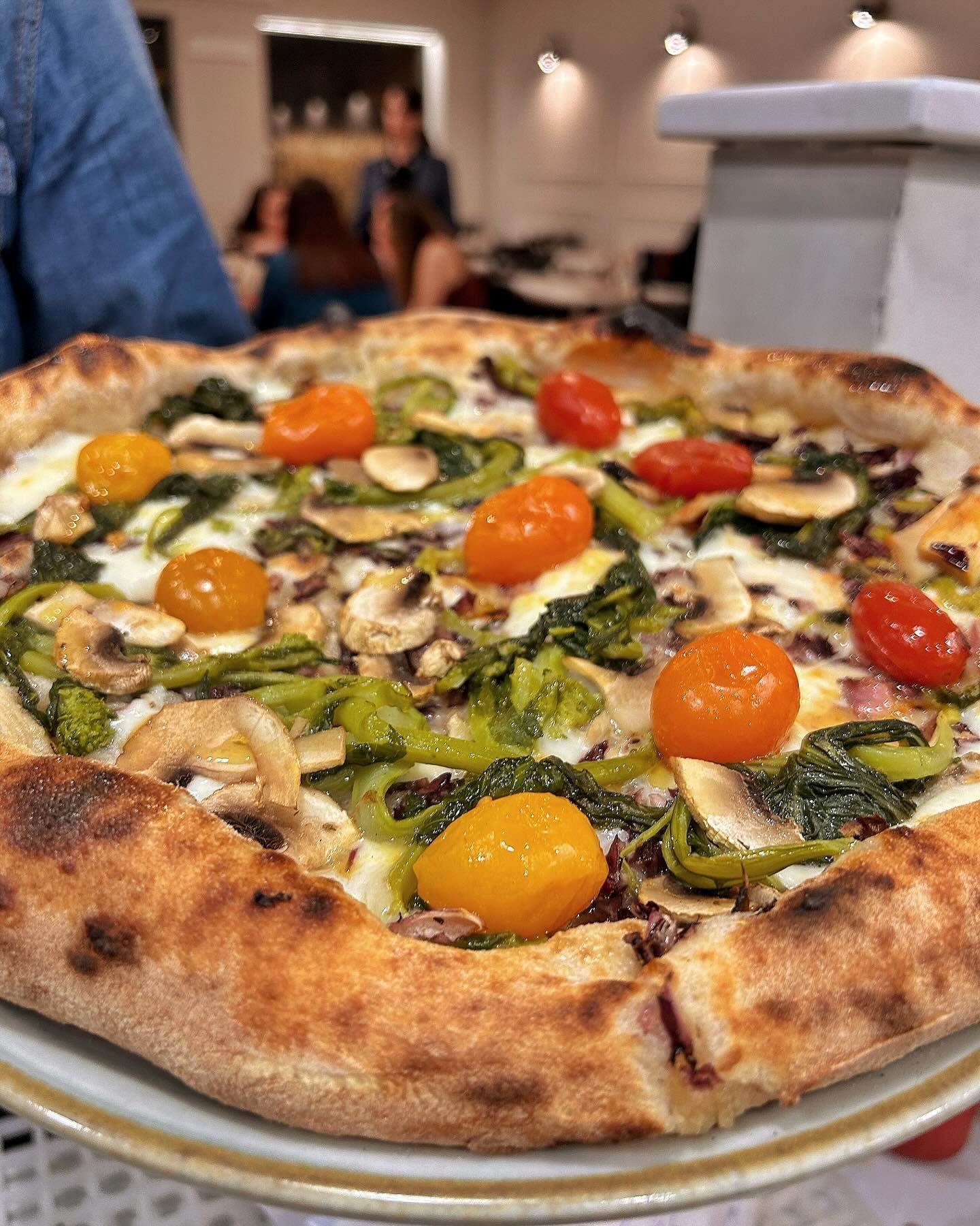 Una pizza con pomodori, funghi, spinaci e formaggio su un piatto.