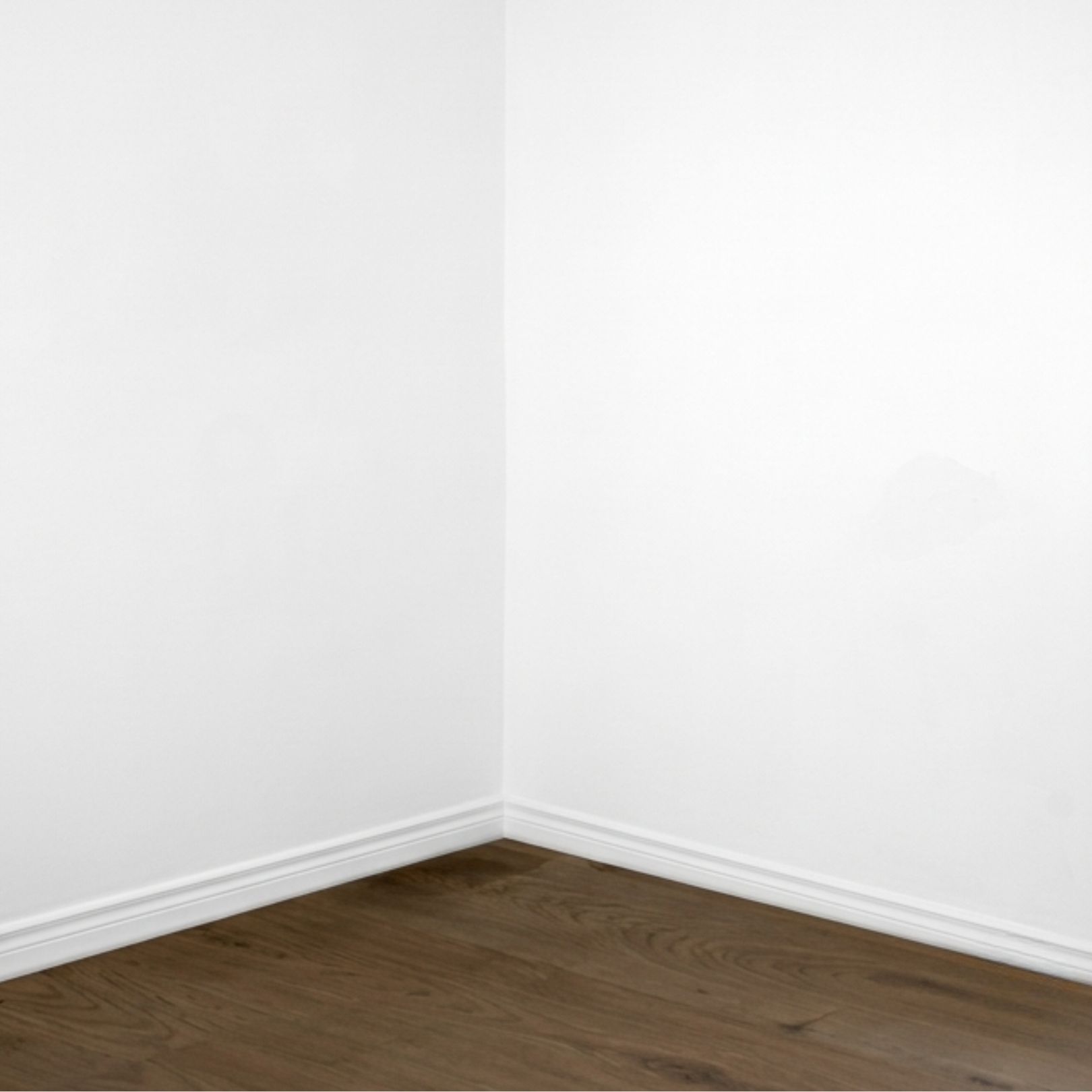 A corner of a room with white walls, white baseboards, and dark wood flooring.