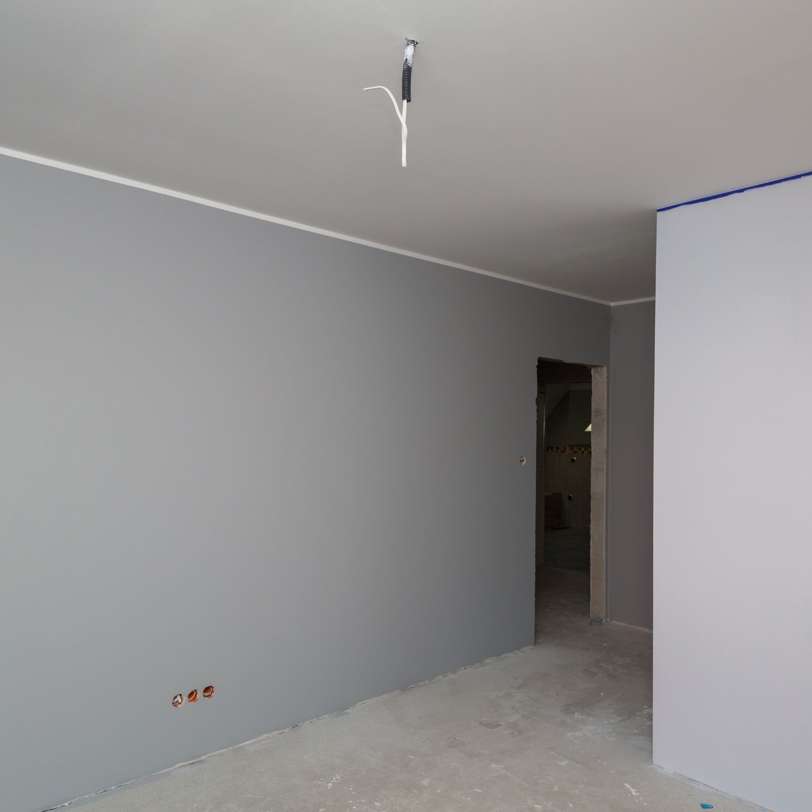 A room under construction with gray painted walls, a white ceiling, exposed electrical wiring, and a doorway.