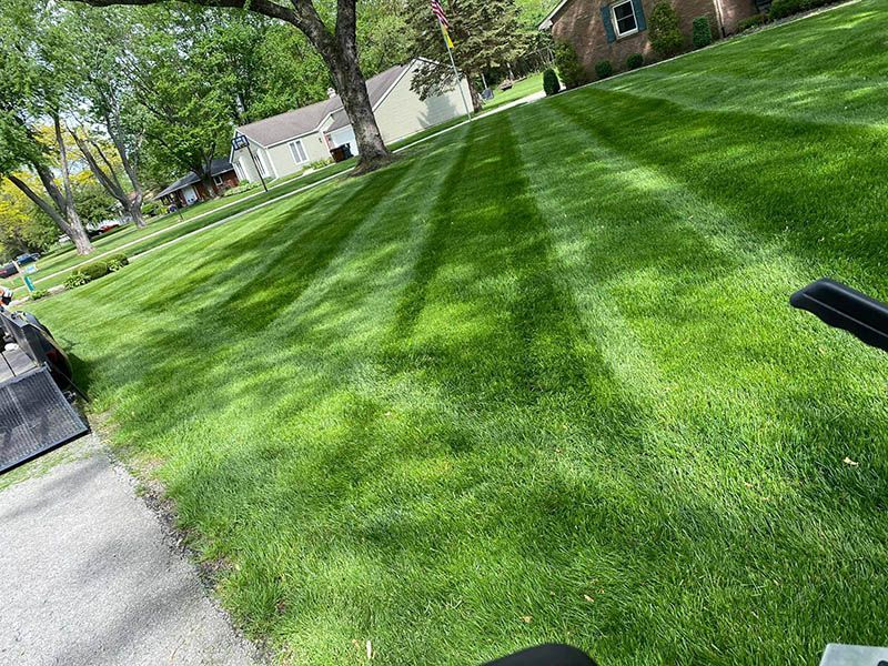 A lawn mower is cutting a lush green lawn in front of a house.
