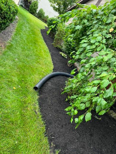 A black pipe is laying on the ground next to a lush green lawn.