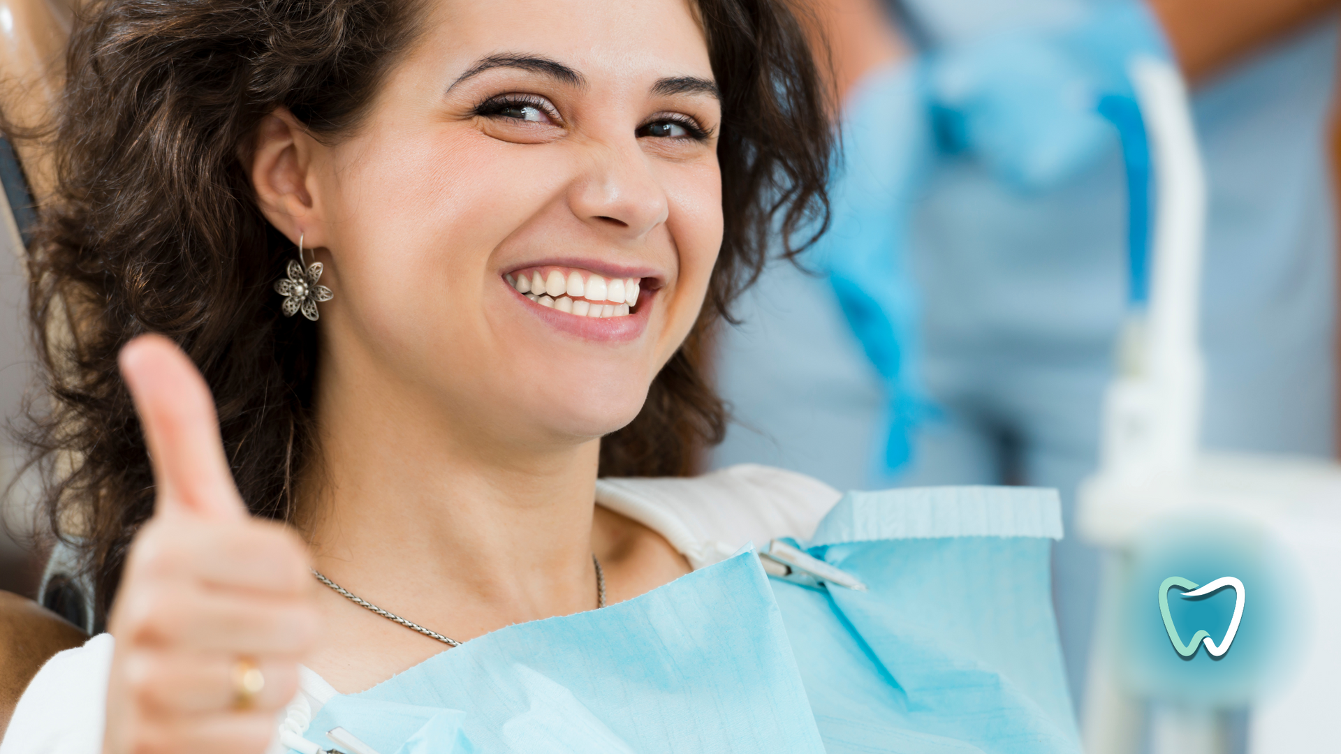 A woman is giving a thumbs up in a dental chair.
