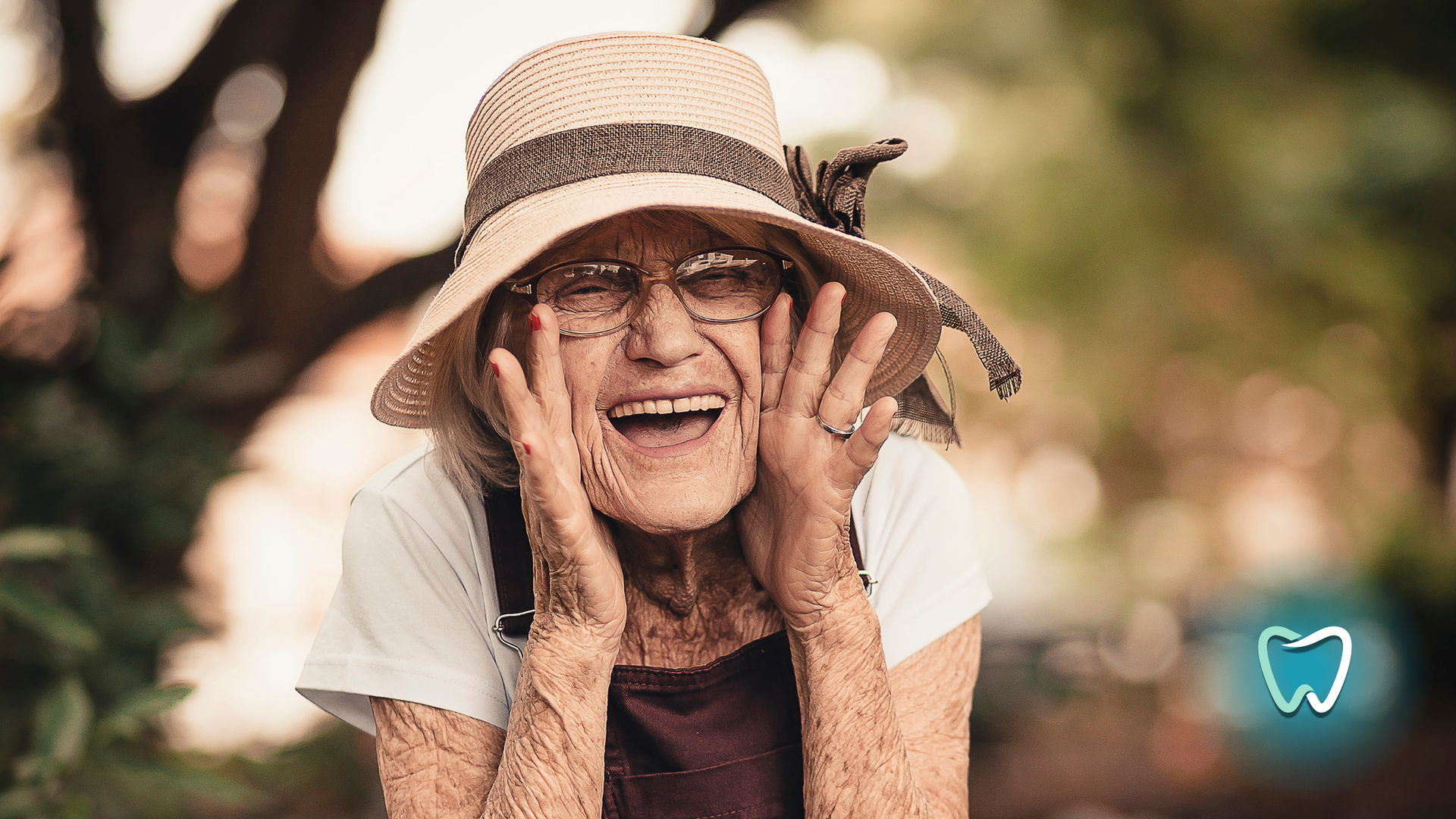 An elderly woman wearing a hat and glasses is smiling.