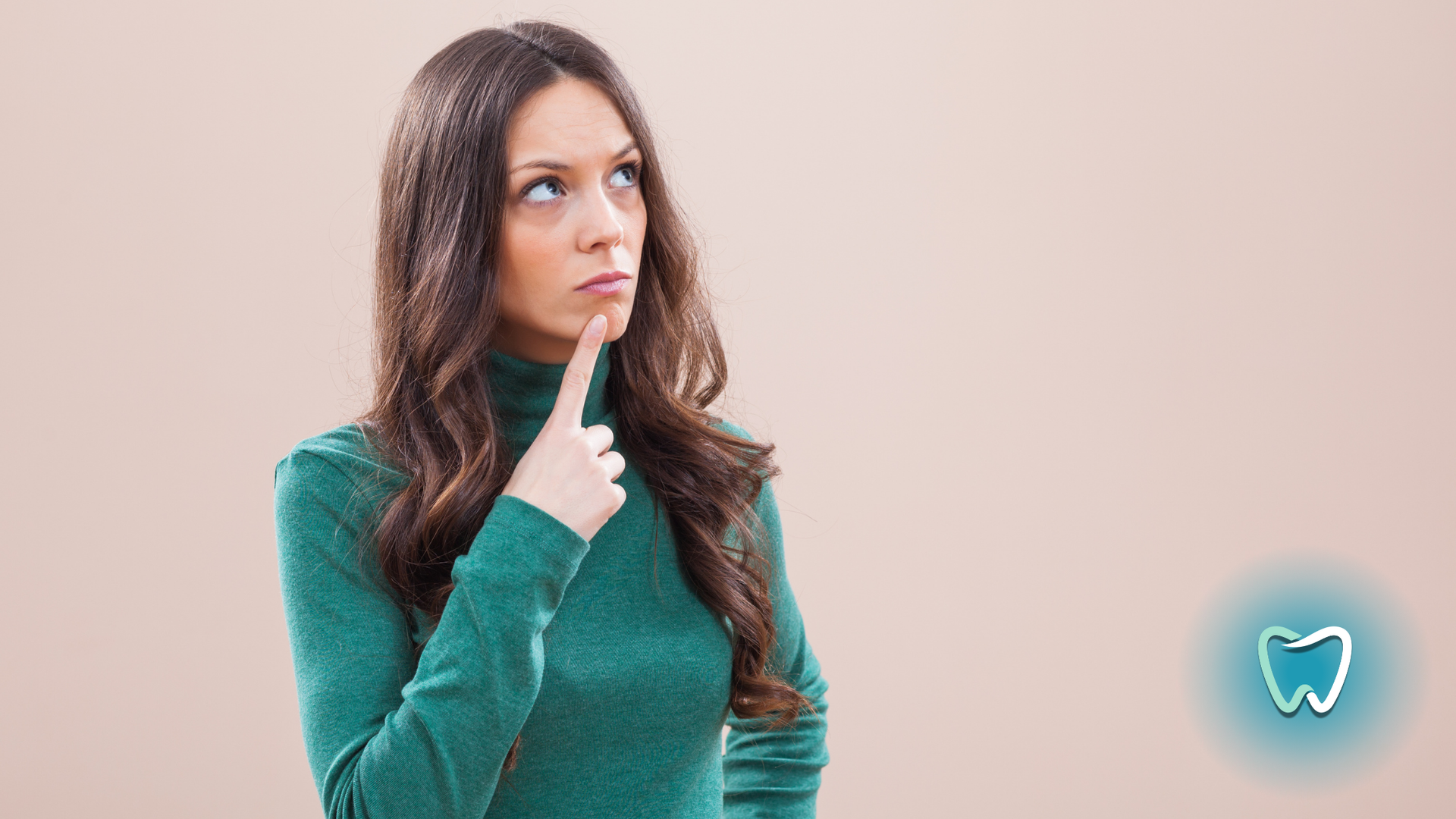 A woman in a green sweater is holding her finger to her chin and looking up.