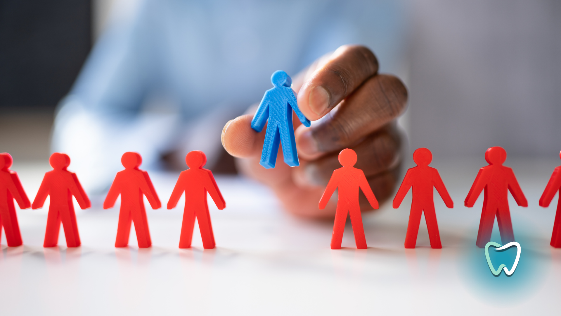 Hand selecting a blue figurine from a row of red figurines, symbolizing choice.