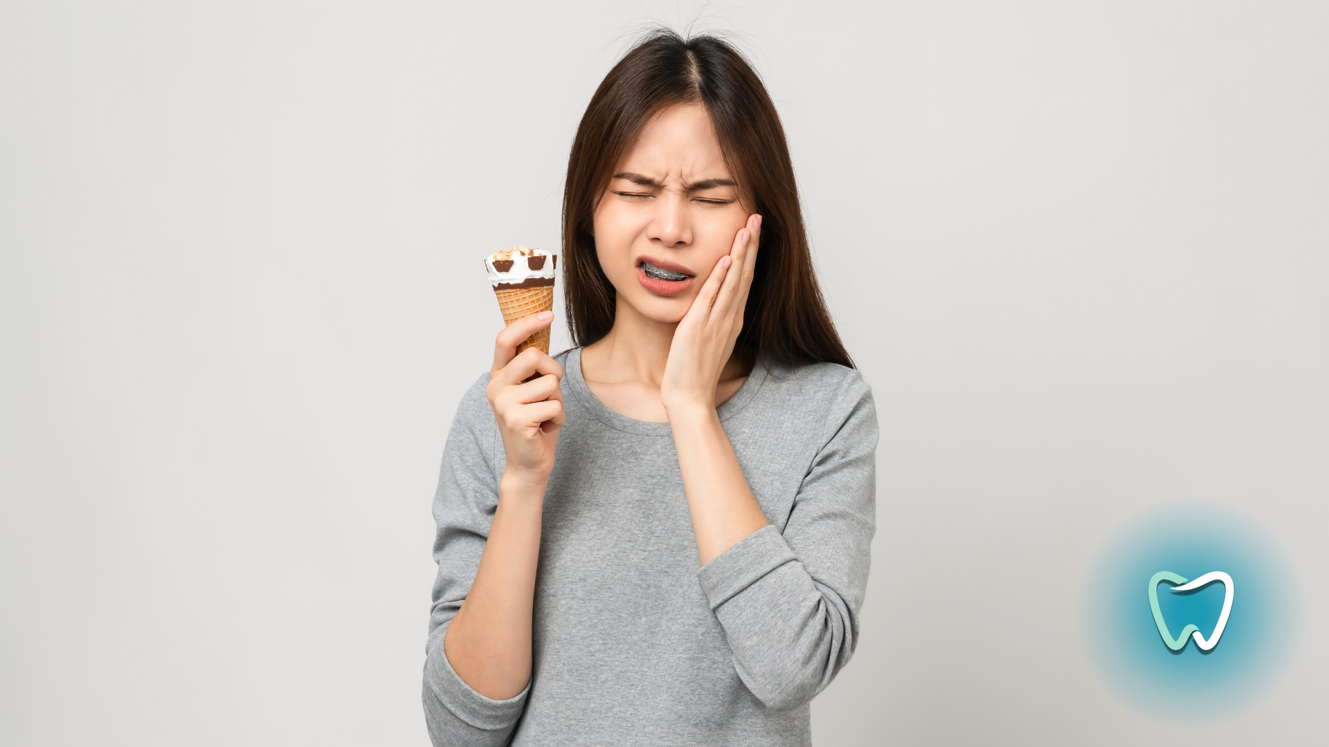 A woman is holding an ice cream cone and having a toothache.