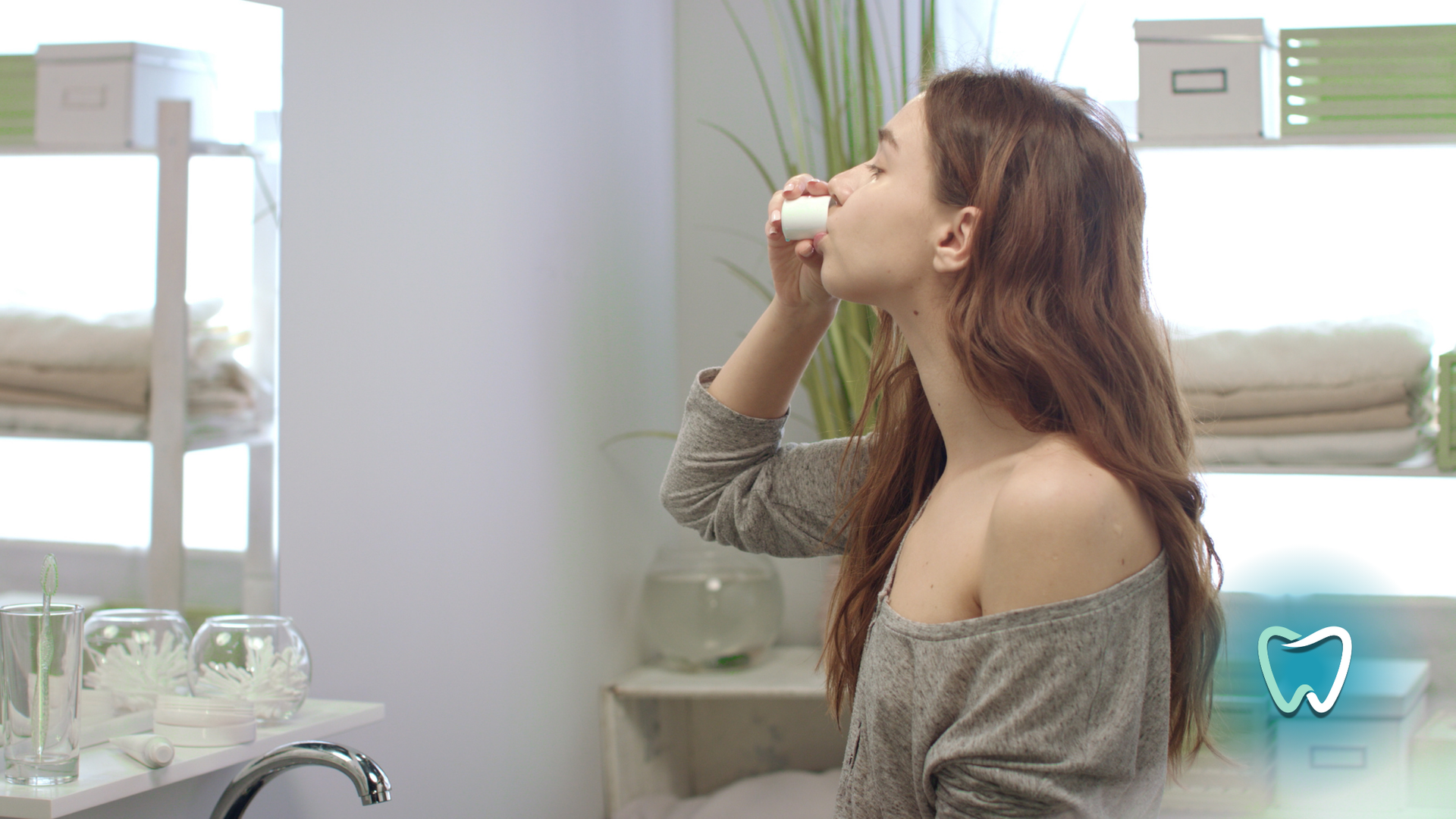 A woman is brushing her teeth in a bathroom in front of a mirror.