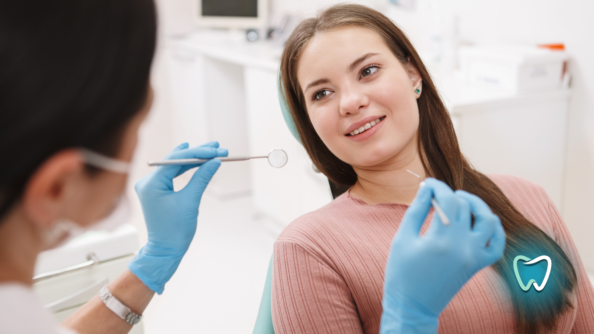 Dentist examining a smiling woman's teeth in a dental office.