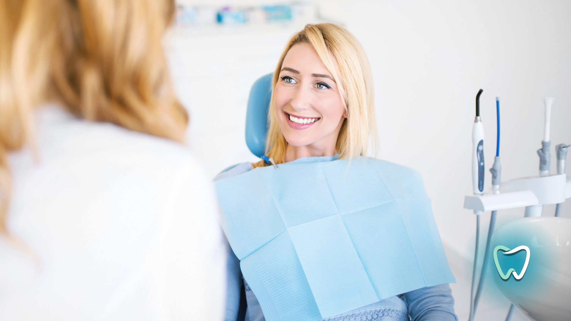 A woman is sitting in a dental chair smiling at the dentist.
