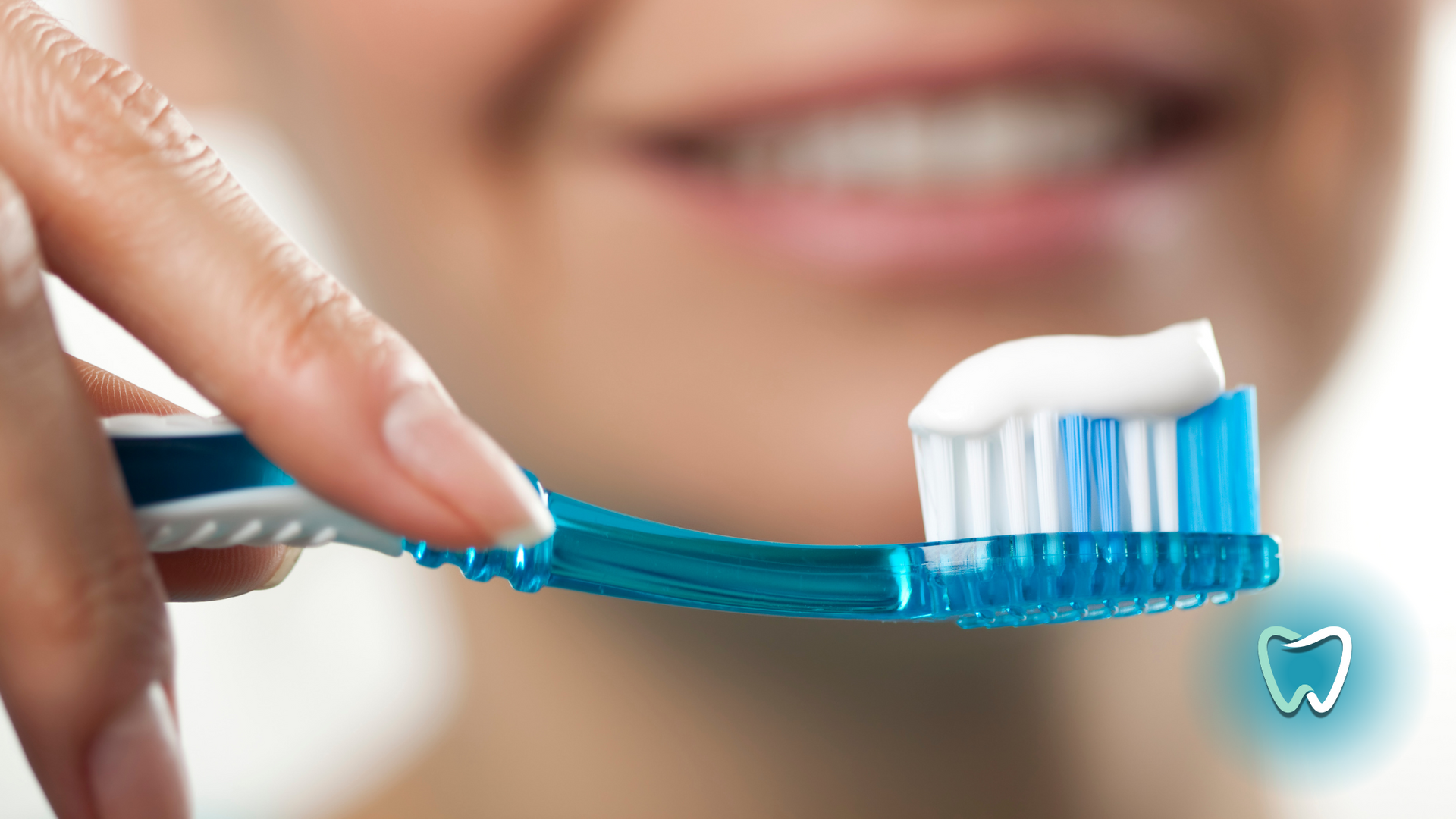 Hand holding toothbrush with toothpaste, smiling person in background.