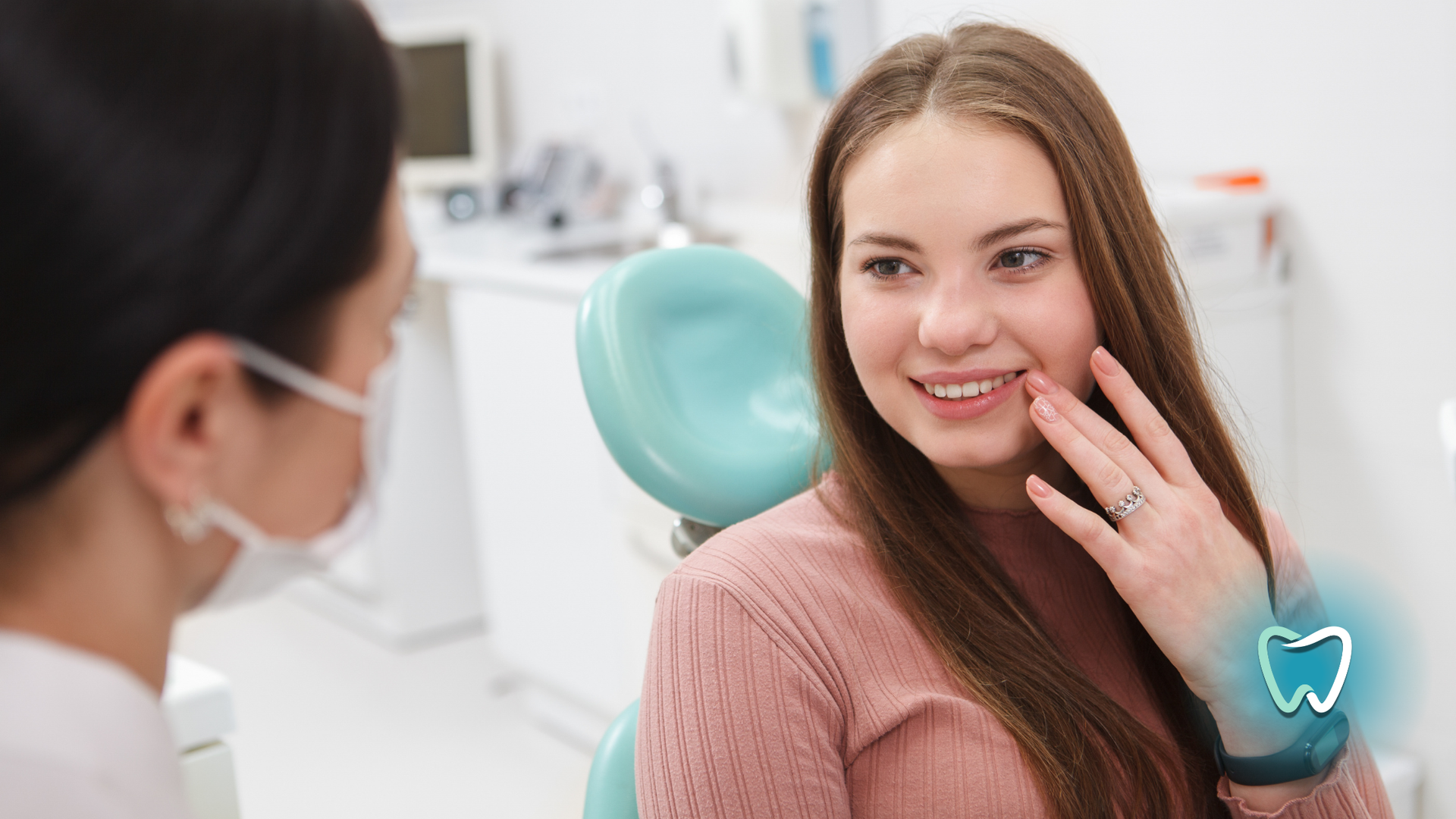Woman in pink sweater at dentist, touching cheek, smiling. Dentist wearing a mask.