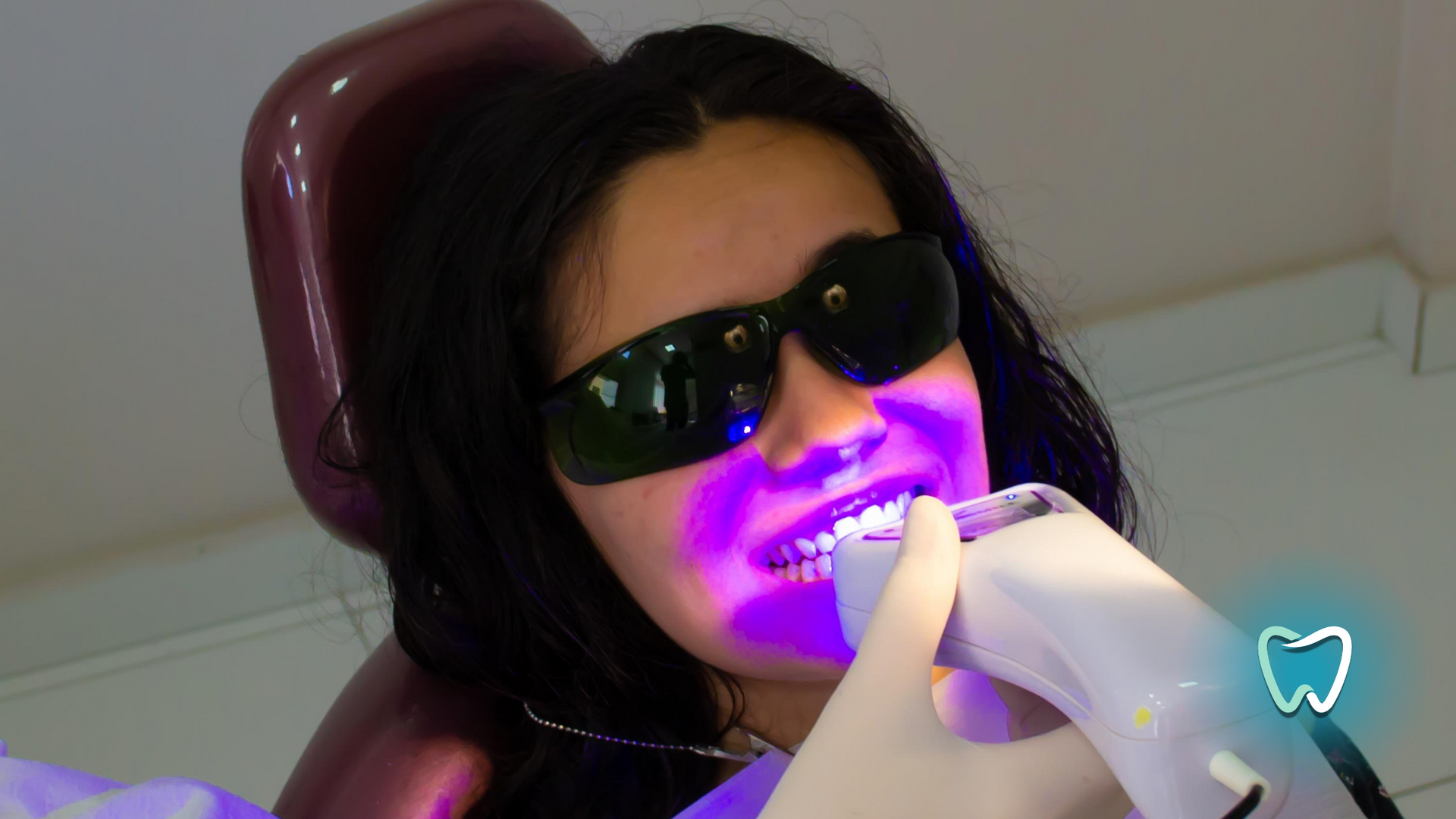 A woman wearing sunglasses is getting her teeth whitened by a dentist.