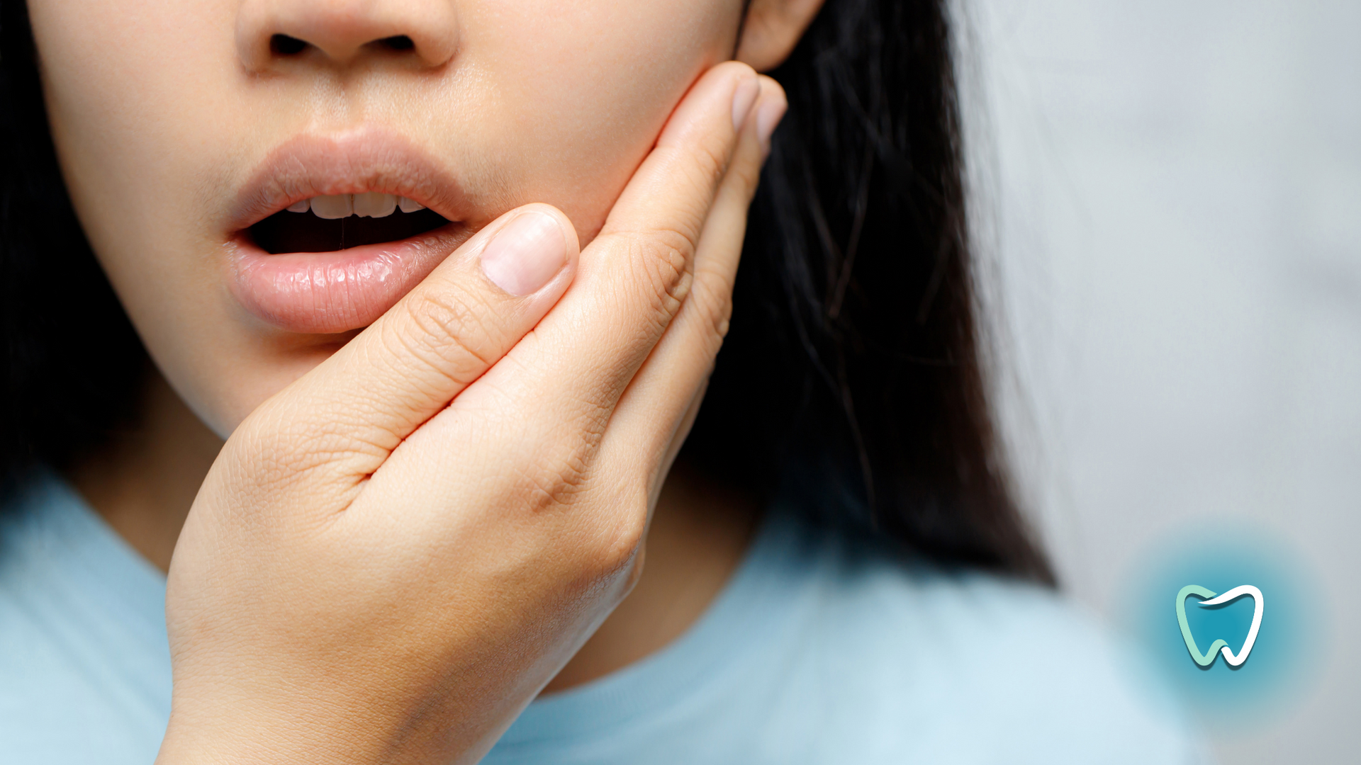 Woman holding her cheek in pain with open mouth, indicated possible toothache.