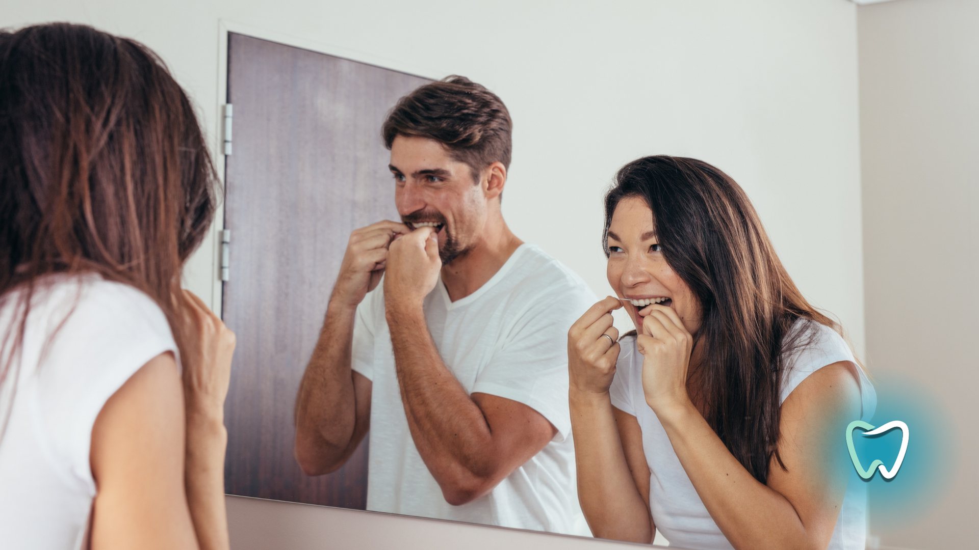 A man and a woman are flossing their teeth in front of a mirror.