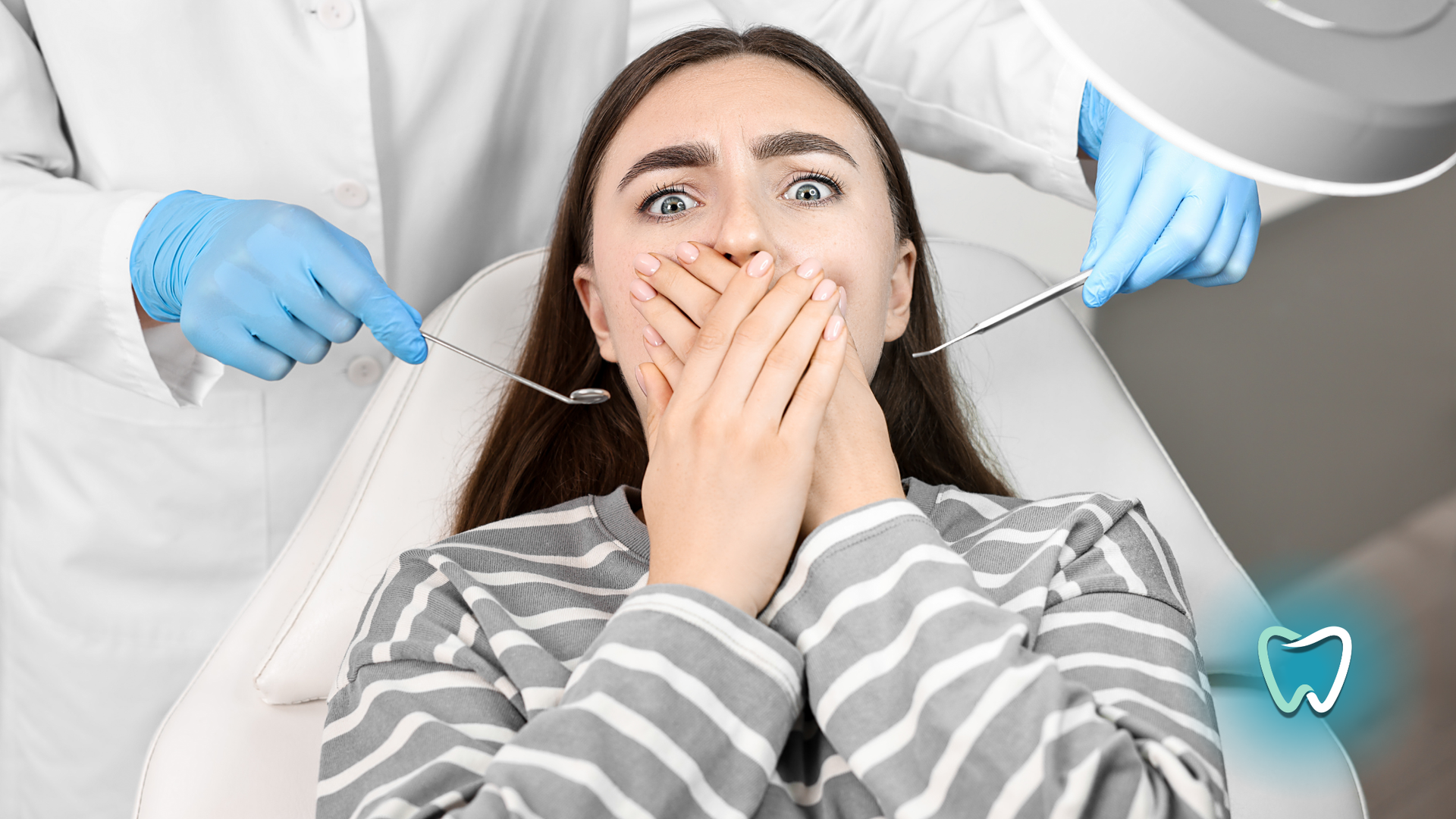 Woman with a fearful expression covers her mouth while dentists reach towards her with tools in a dental chair.
