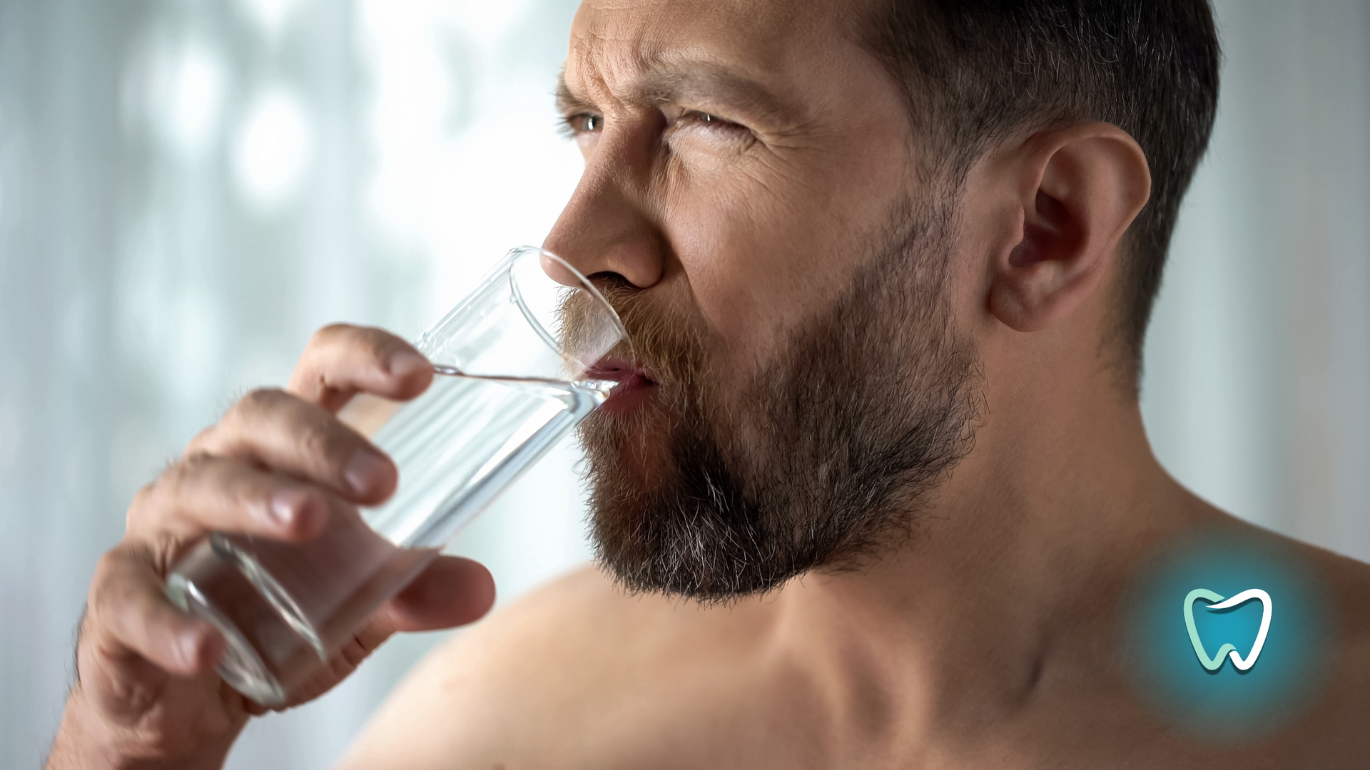 A man with a beard is drinking a glass of water.