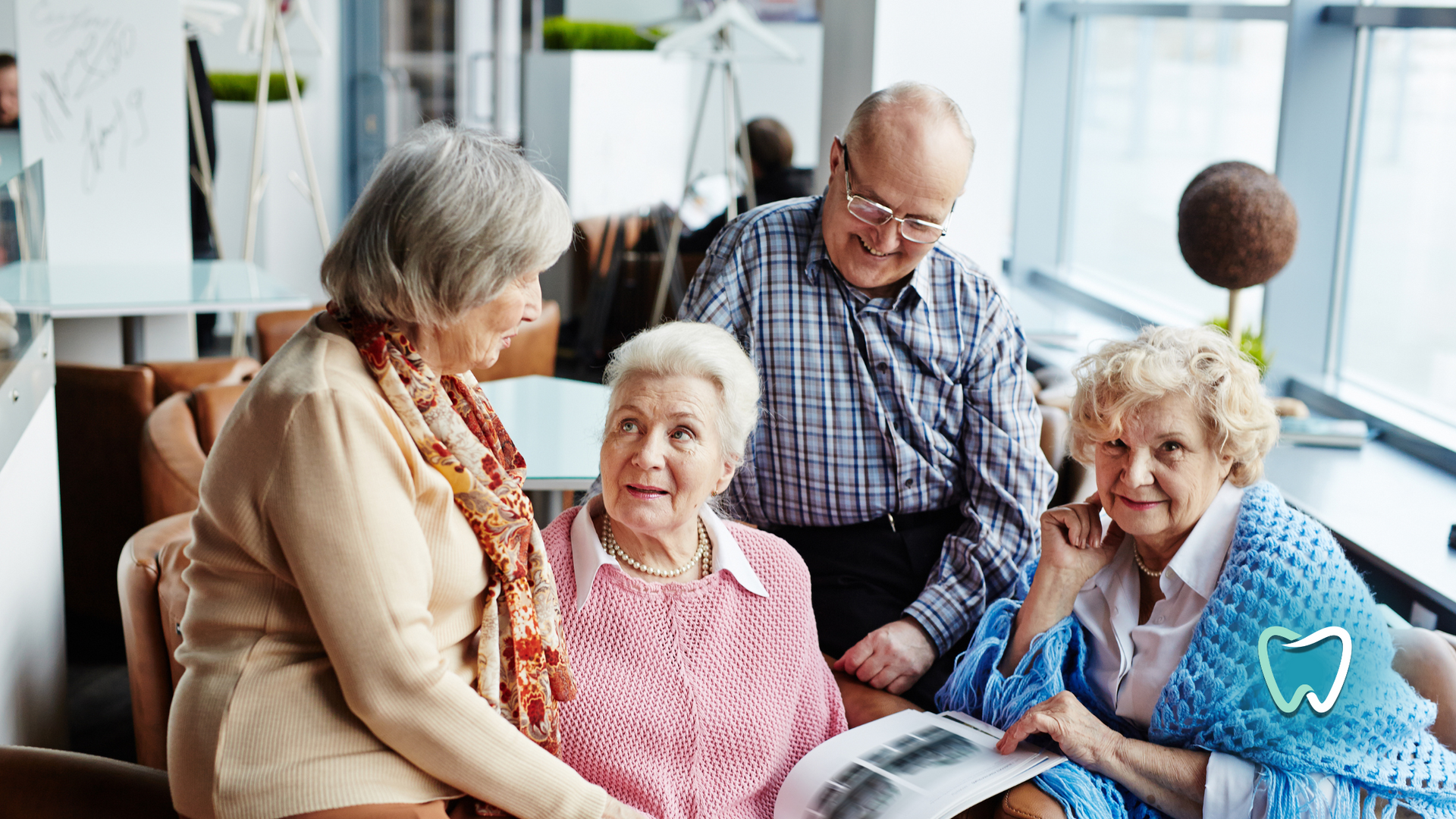 A group of elderly people are sitting around a table looking at a magazine.