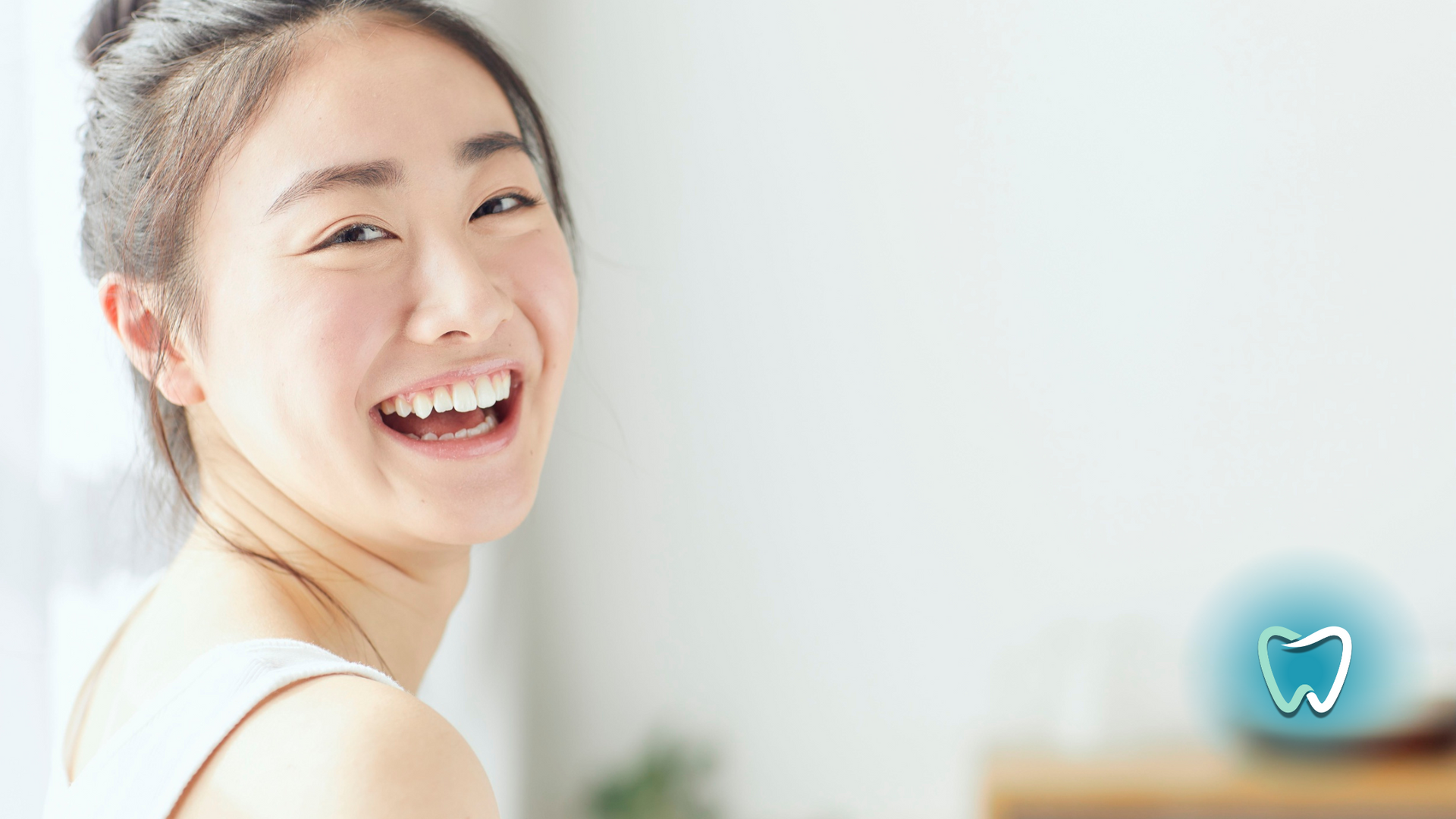 Smiling Asian woman with bright teeth, white background, dental logo in the corner.