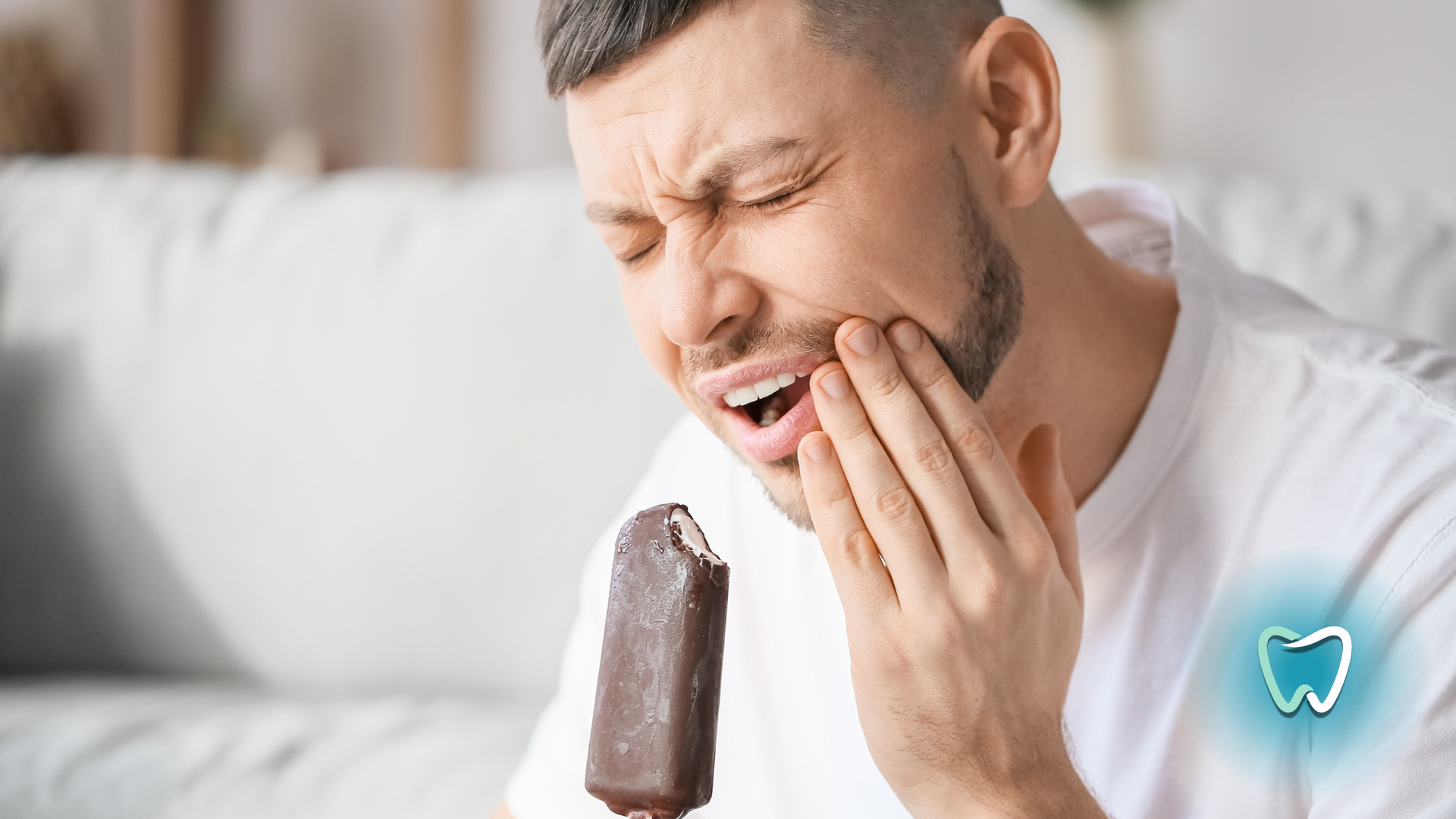A man is eating an ice cream bar and has a toothache.