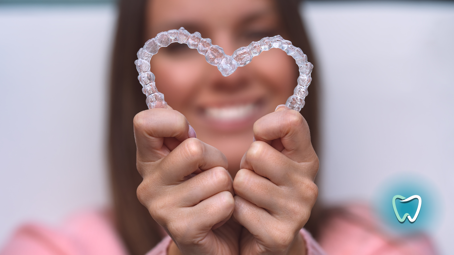 Woman holding clear dental aligners in a heart shape, smiling with teeth visible.