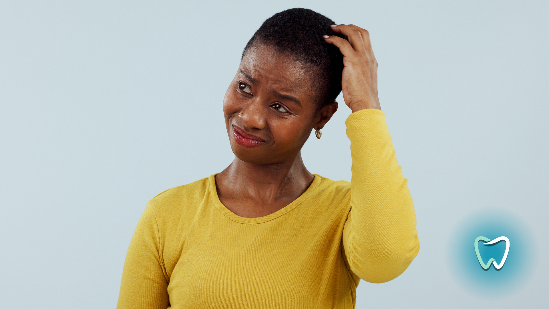A woman in a yellow shirt is scratching her head.