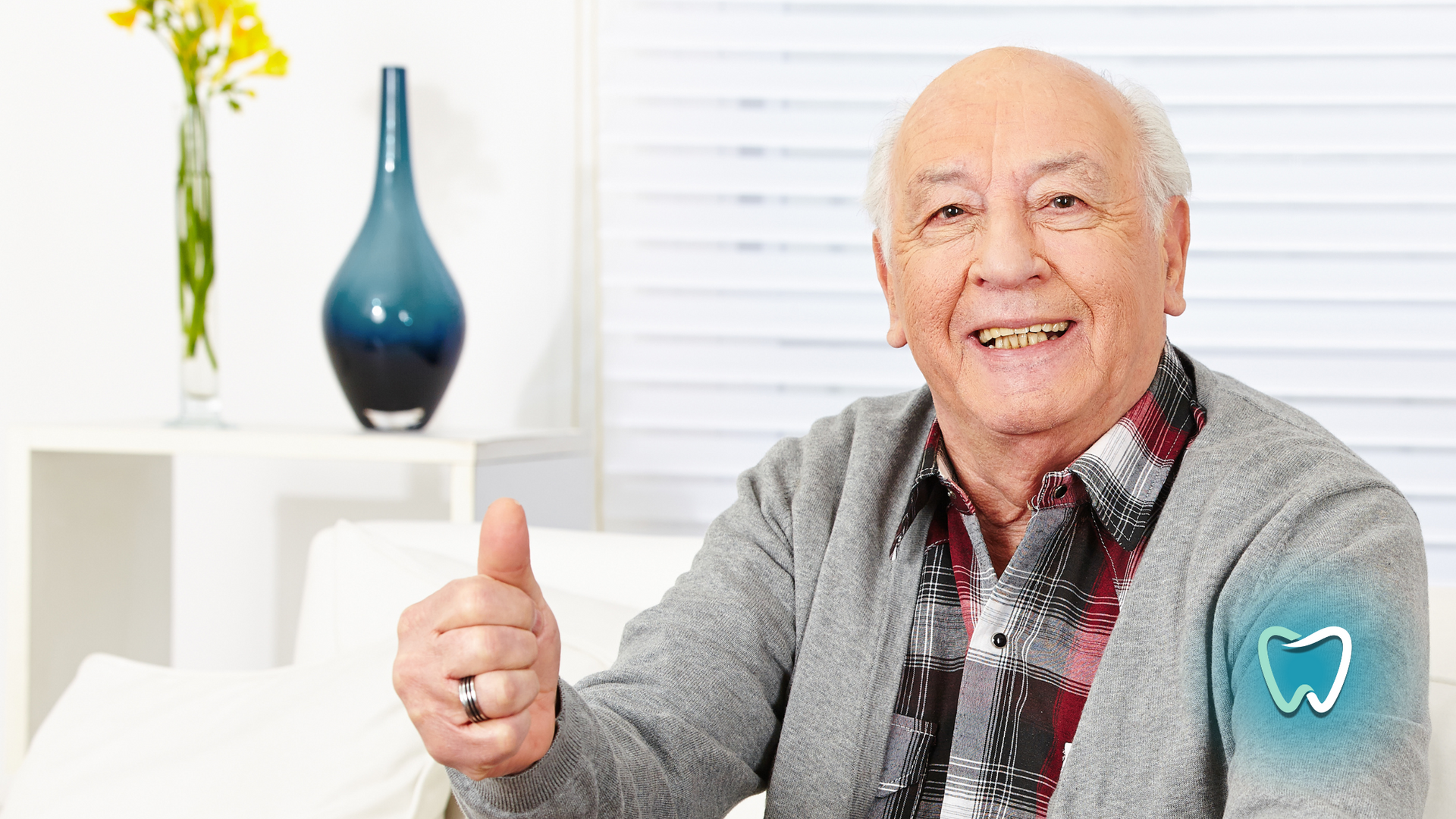 An elderly man is giving a thumbs up sign while sitting on a couch.