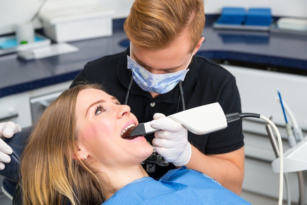 A woman is sitting in a dental chair while a dentist takes a picture of her teeth.