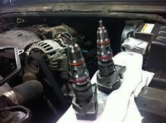 Two fuel injectors are sitting under the hood of a car.