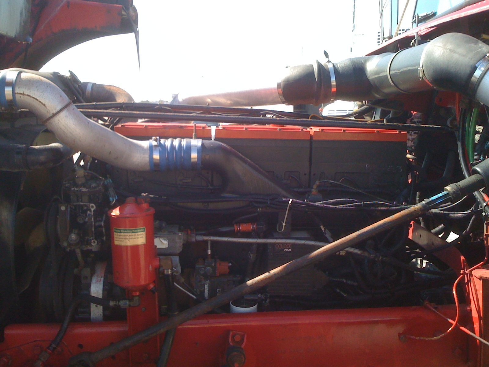 The engine of a red semi truck is shown with the hood open.