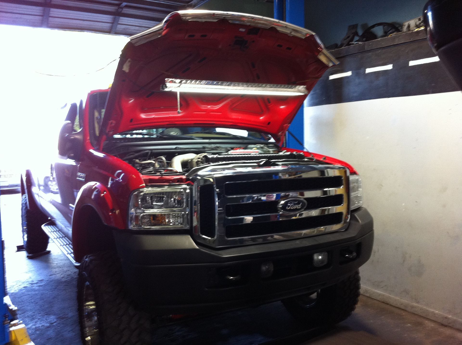 A red ford truck with its hood open in a garage