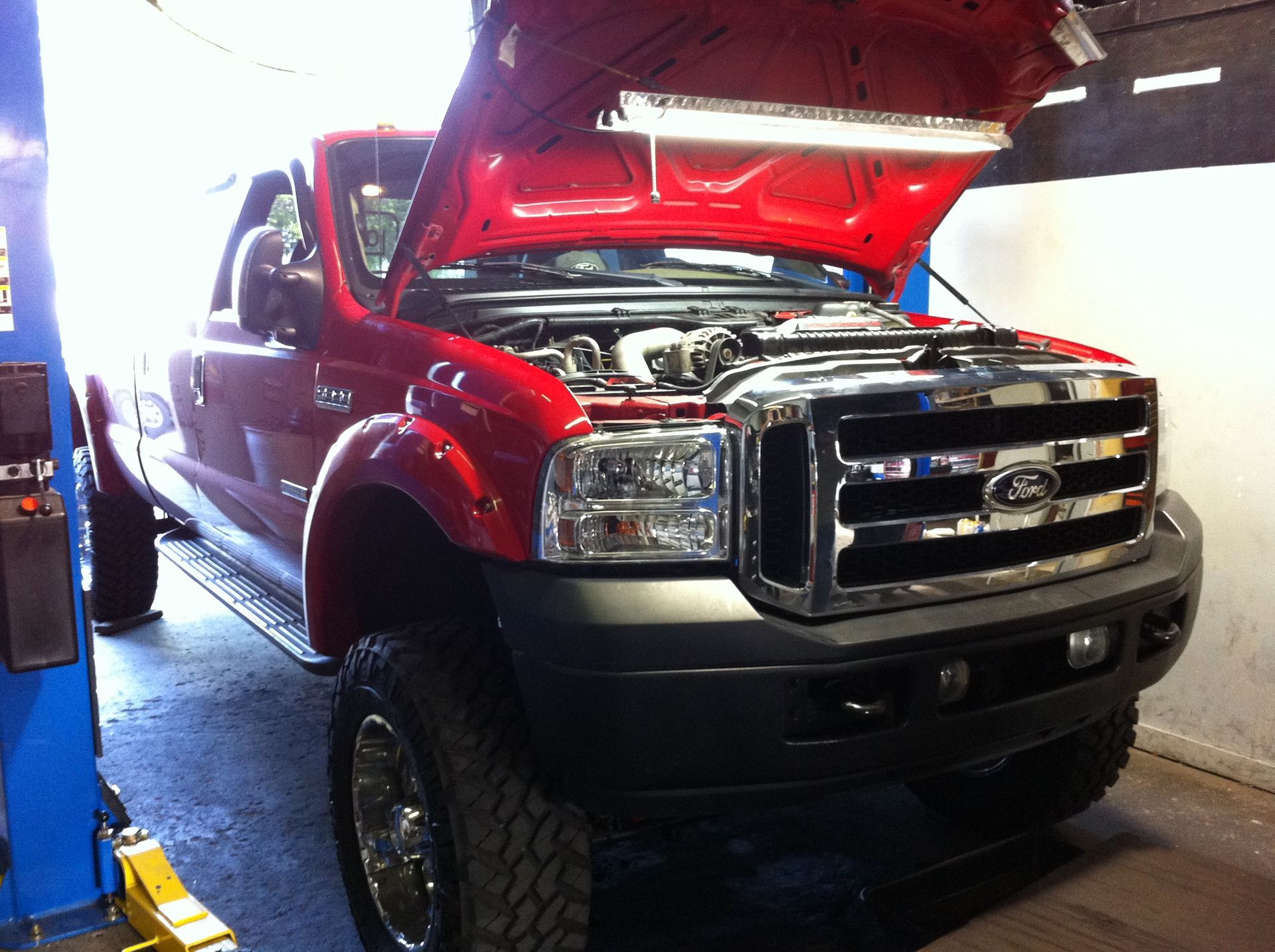 A red ford truck with its hood open in a garage