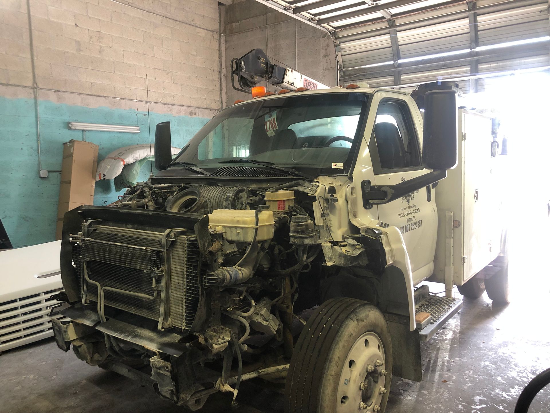 A white truck is sitting in a garage with its engine removed.