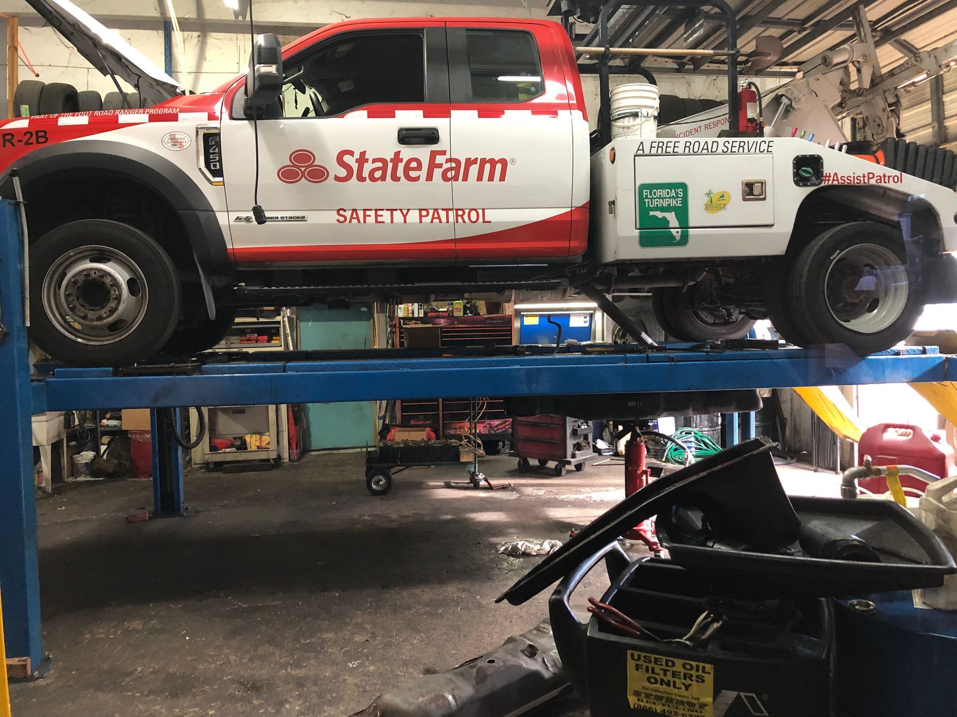 A state farm tow truck is sitting on a lift in a garage.