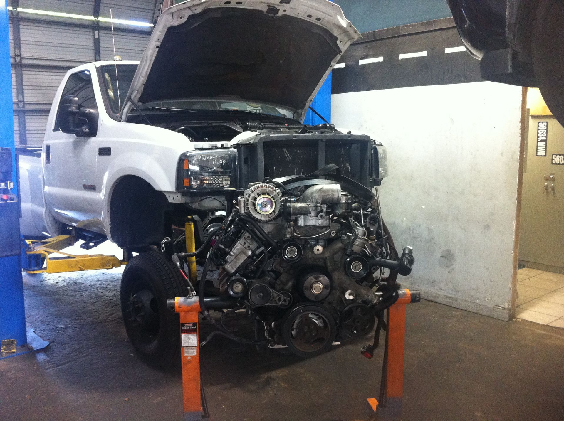 A white truck with the hood open is being worked on in a garage