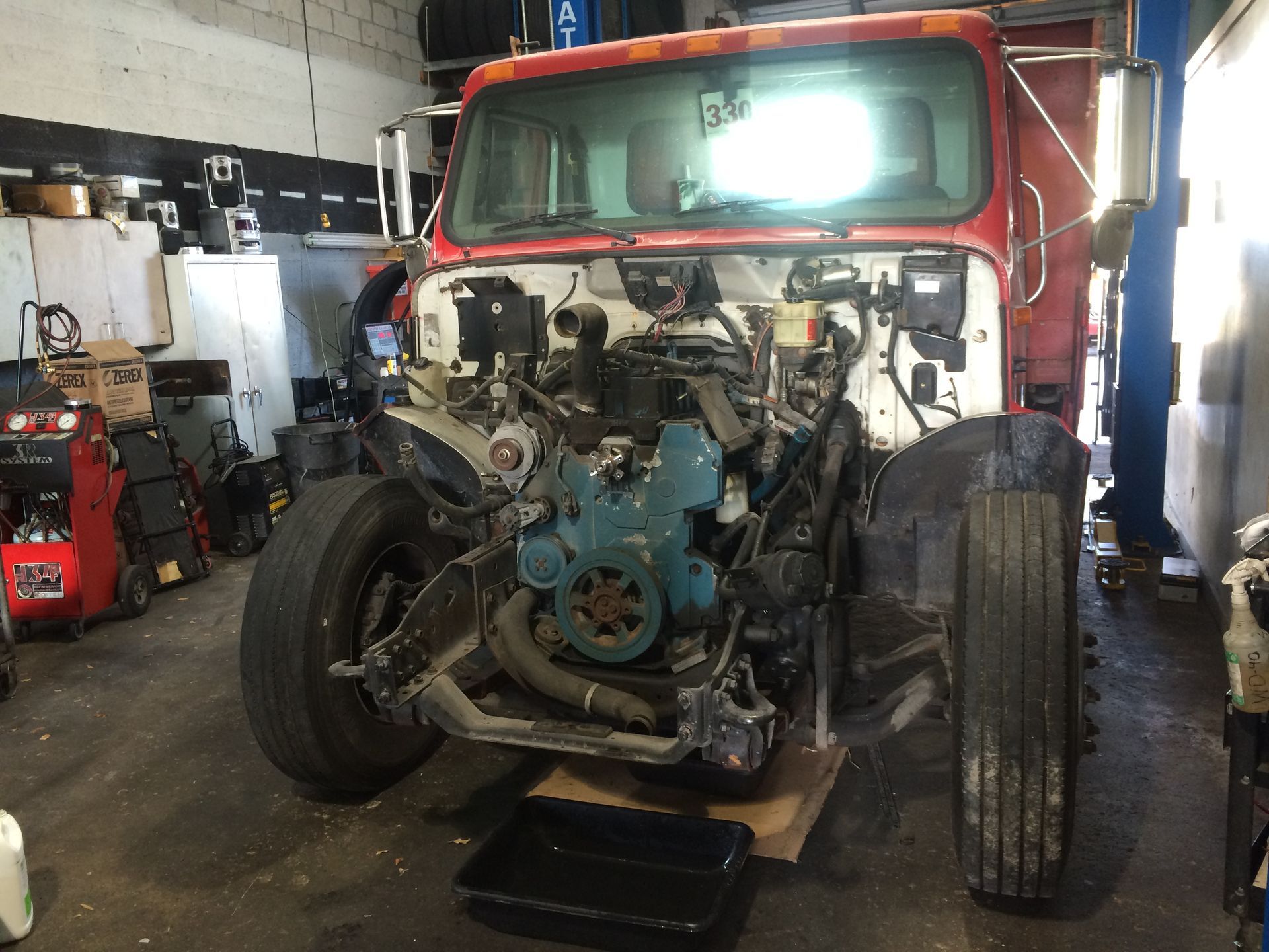 A red truck with the engine removed is in a garage