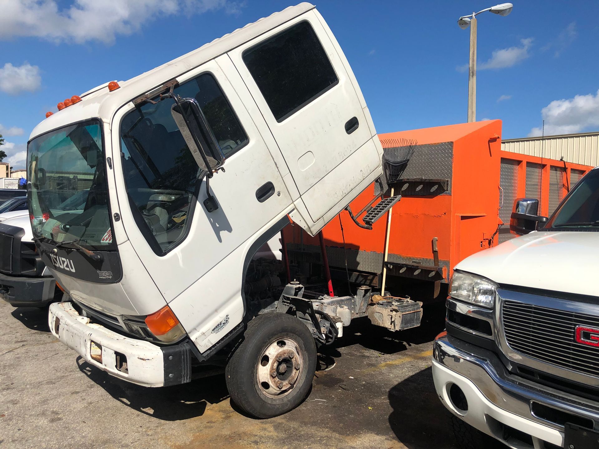 A white truck with its hood up is parked next to a gm truck.