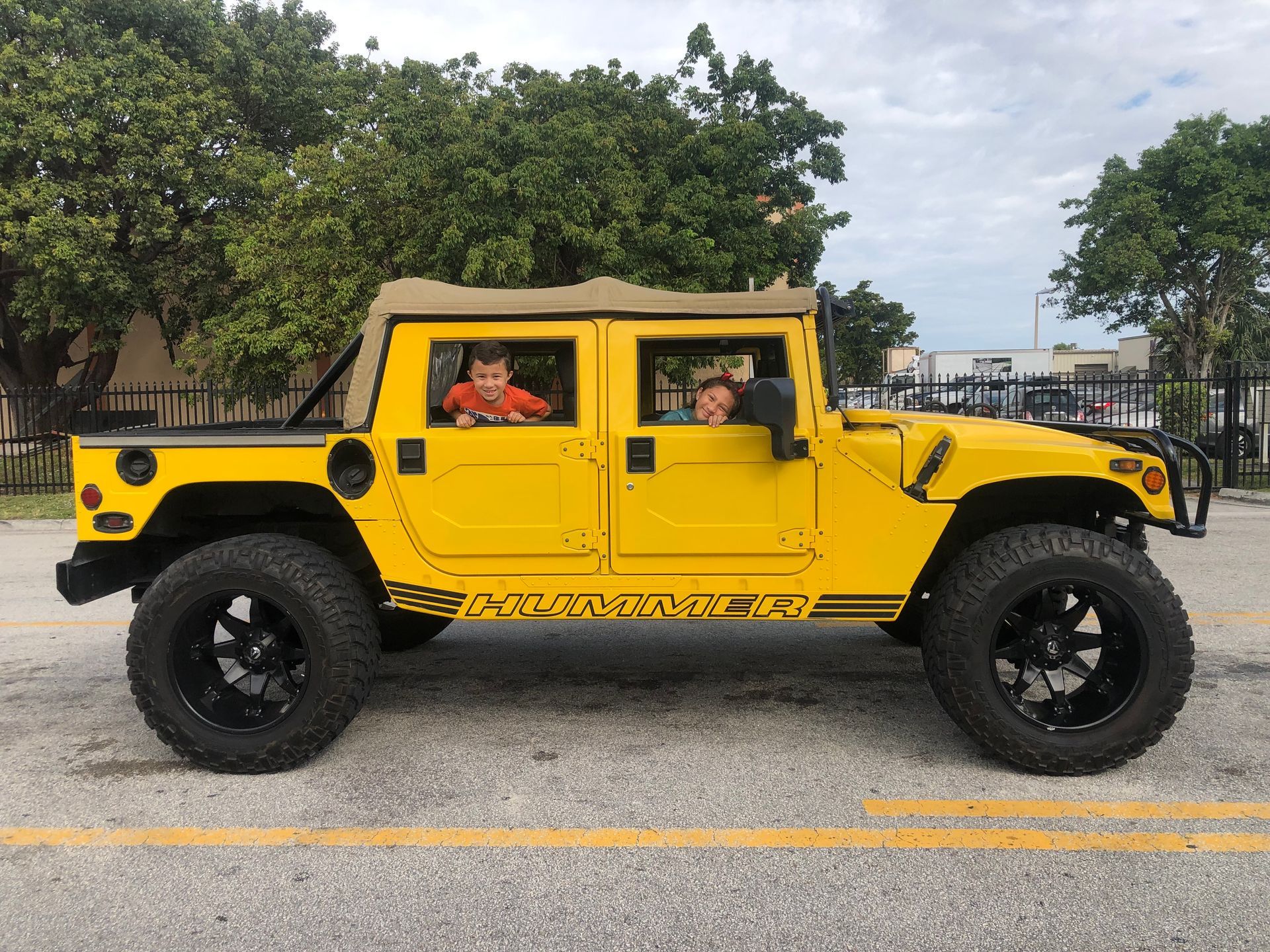 Two children are sitting in the back of a yellow jeep.