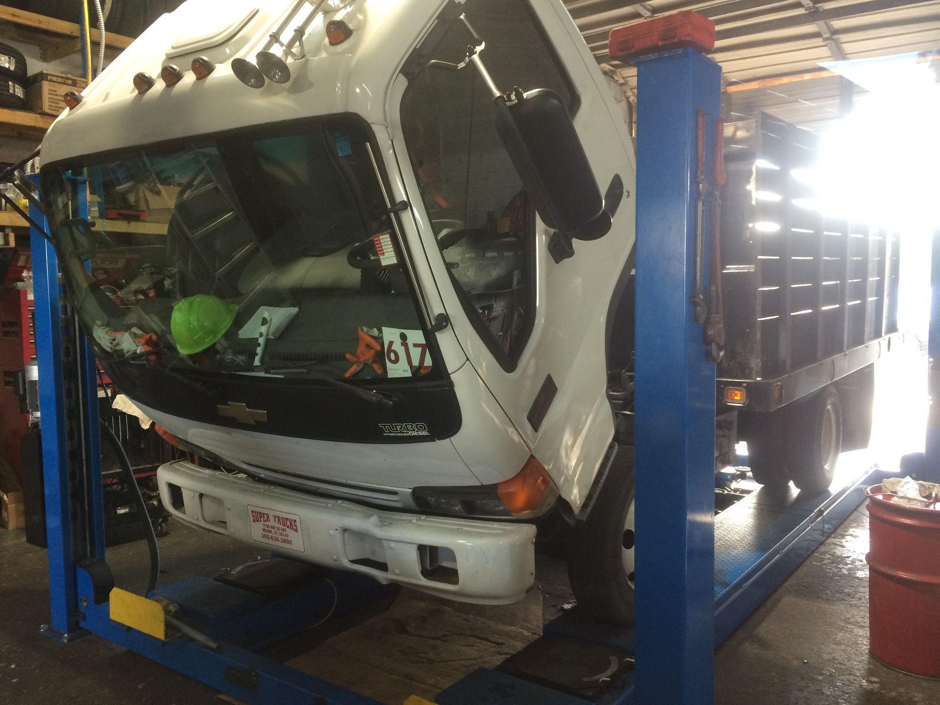 A white truck with the hood up is on a lift in a garage.