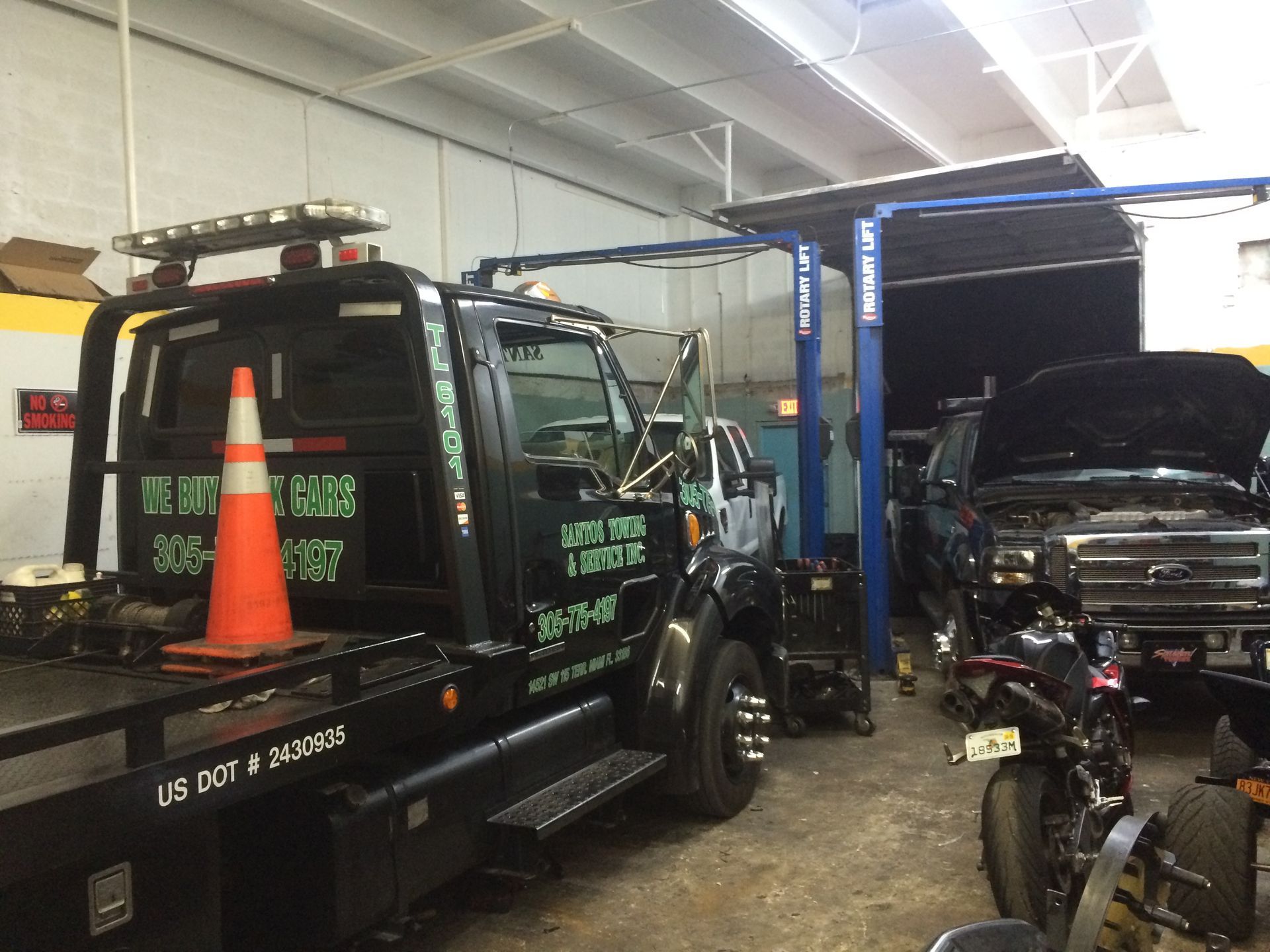 A tow truck is parked in a garage next to a motorcycle.