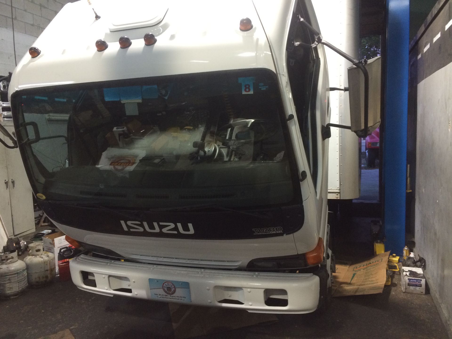 A white isuzu truck is sitting on a lift in a garage.