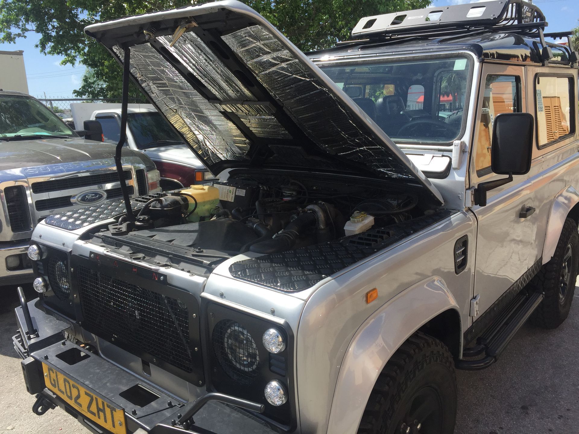 A silver jeep with the hood up is parked in a parking lot.