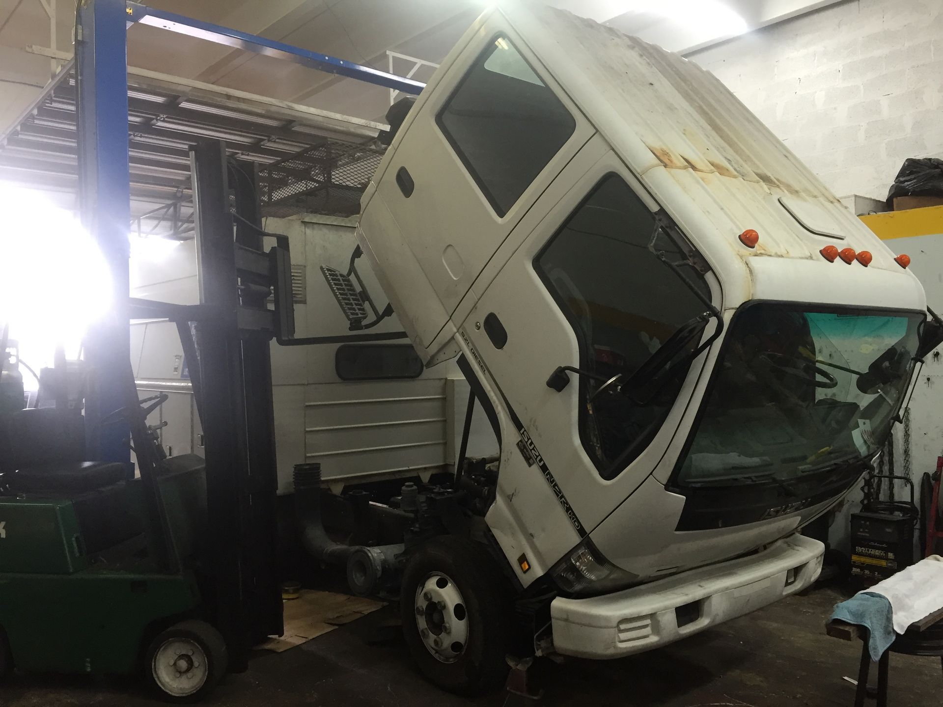 A white truck with its hood up is sitting in a garage next to a forklift.