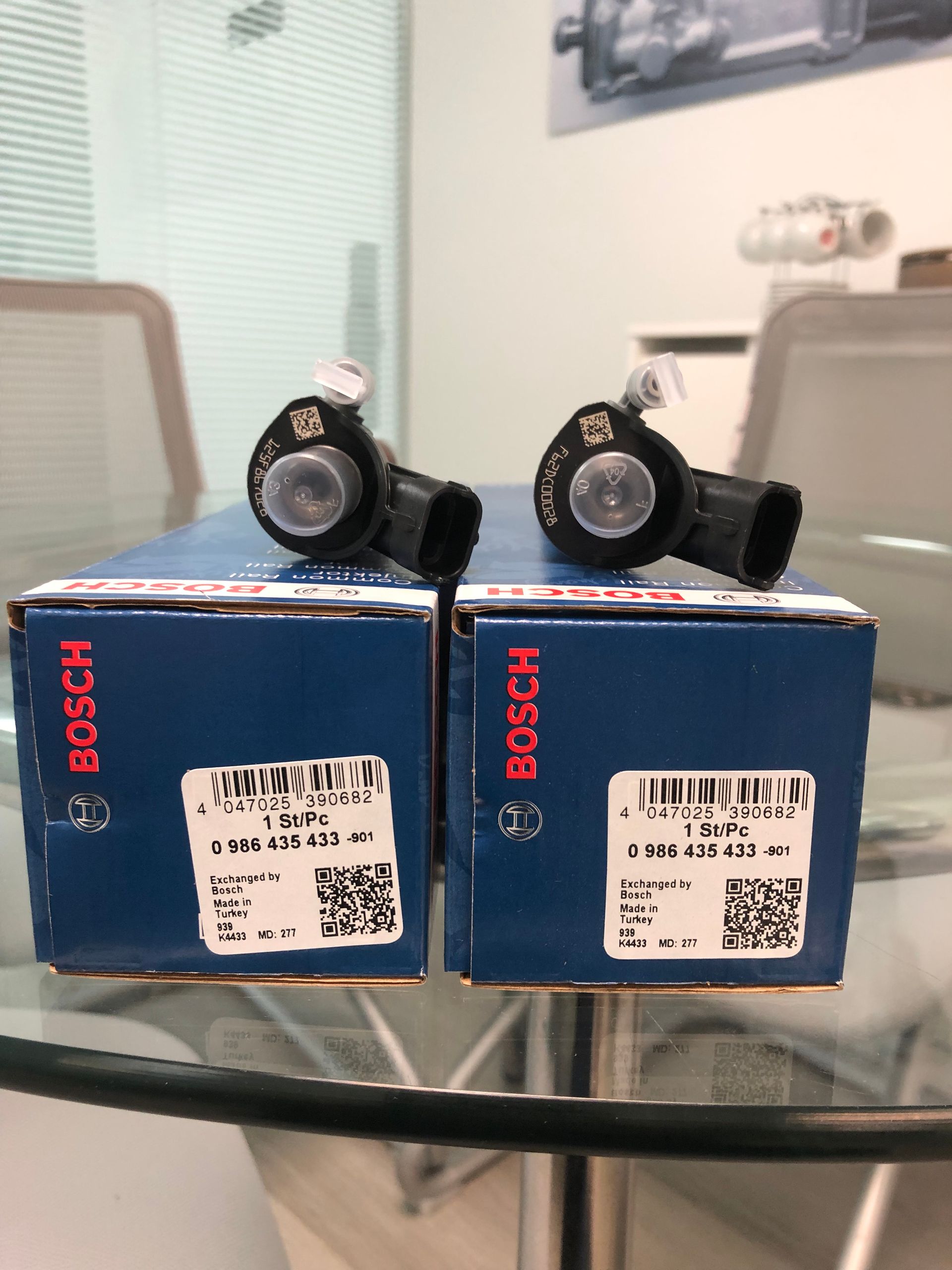 Two boxes of bosch fuel injectors are sitting on a glass table.