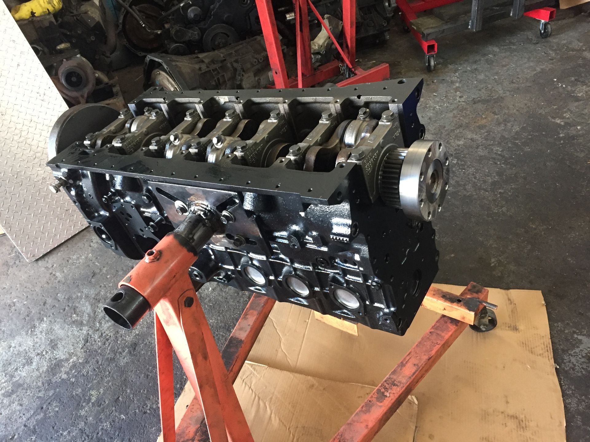 A black engine block is sitting on top of a cardboard box on a stand.