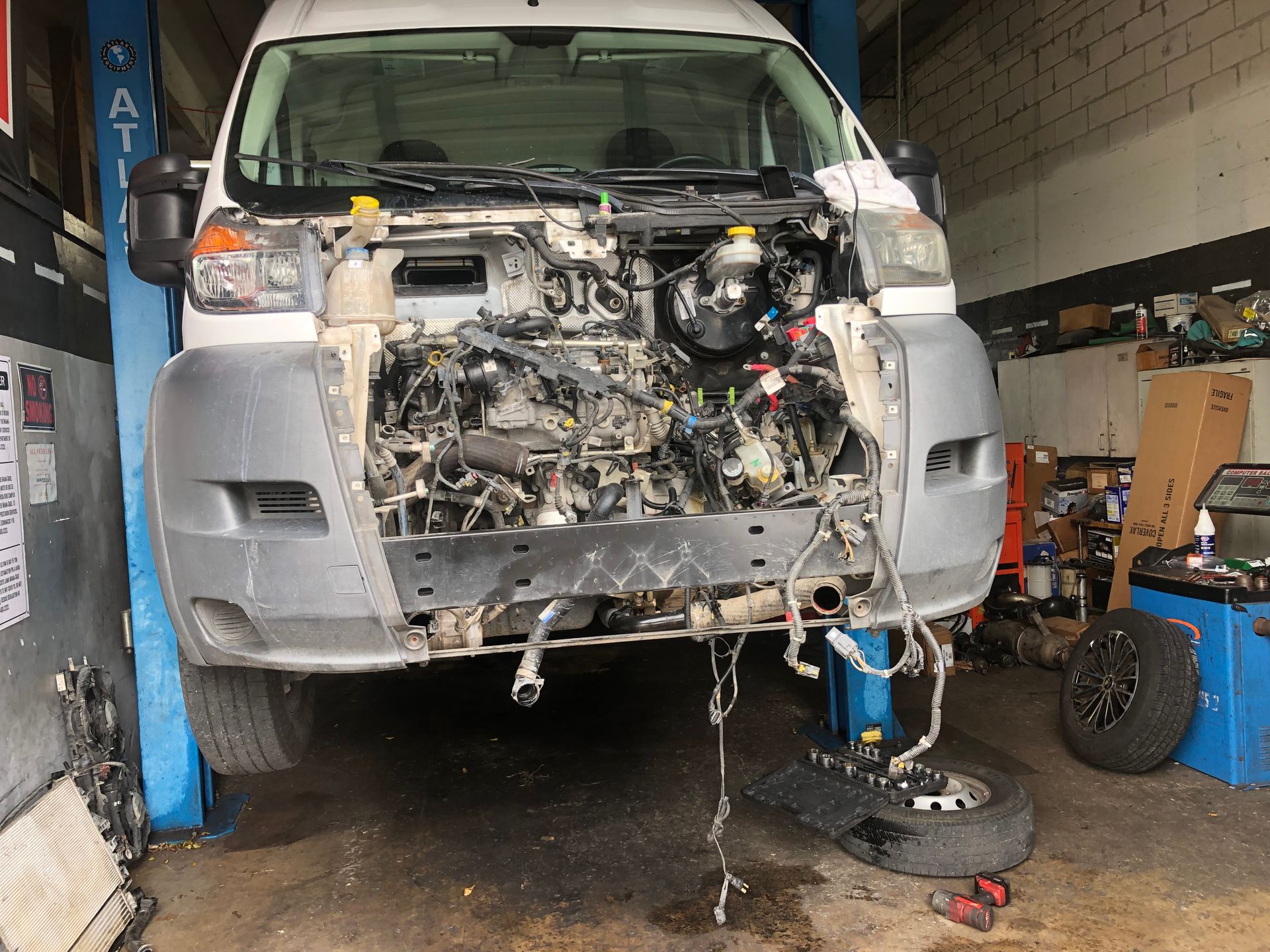 A white van with the hood up is sitting on a lift in a garage.