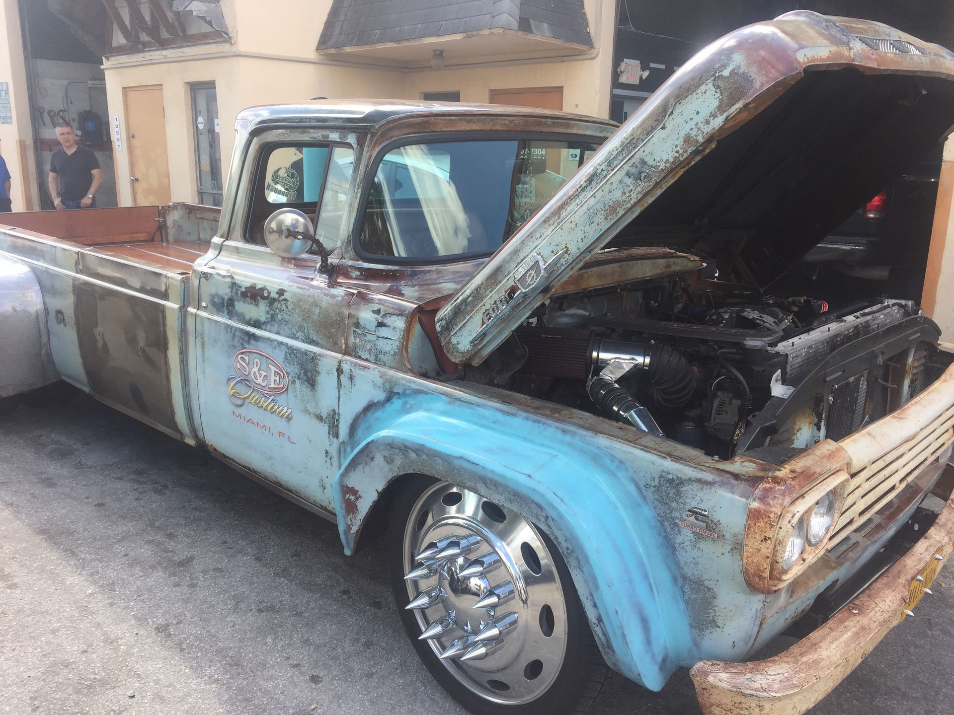 A blue truck with the hood open is parked in front of a building.